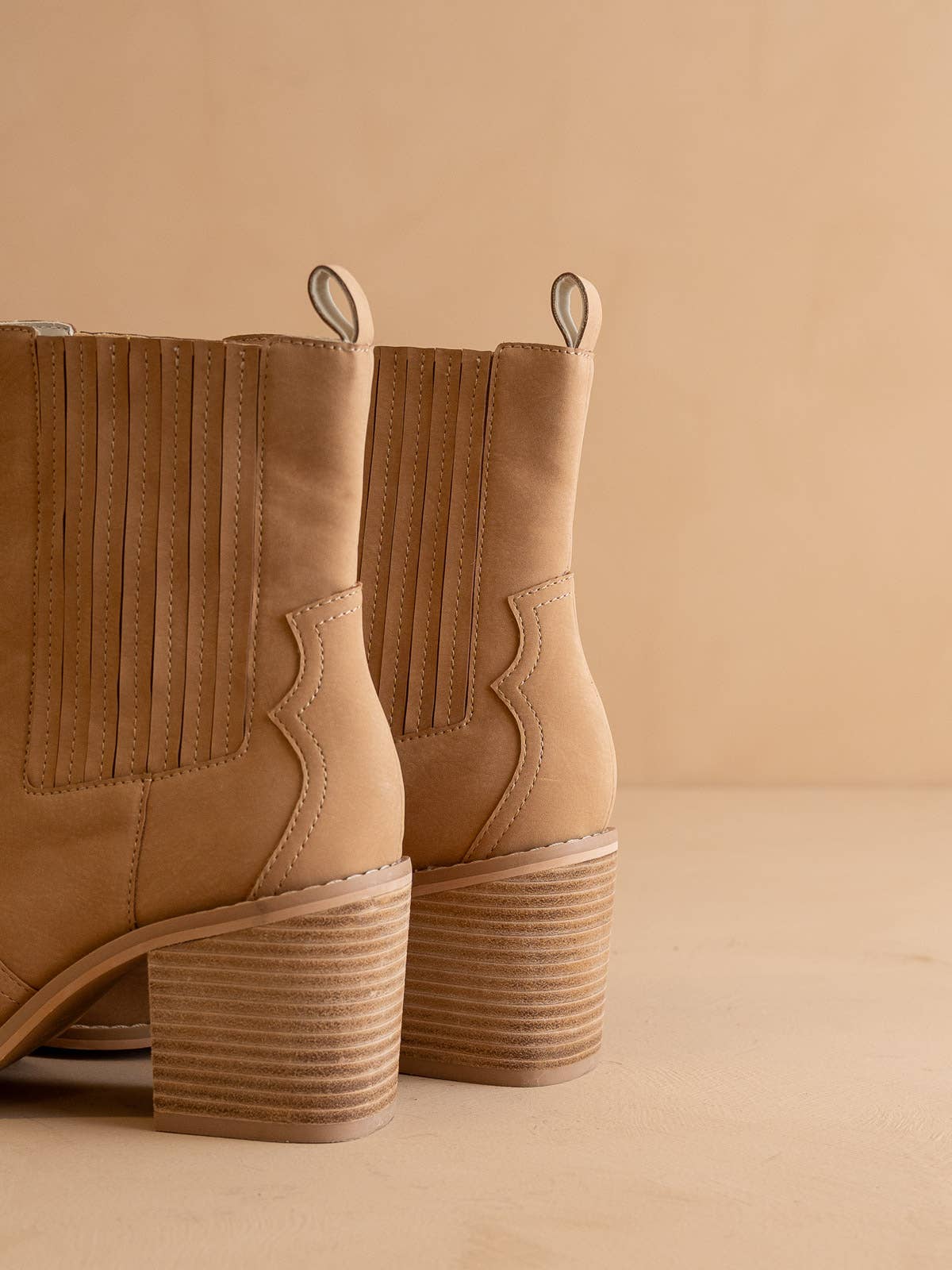 Back view of tan western ankle boots showing stacked block heels, pull tabs, and ribbed side panels.
