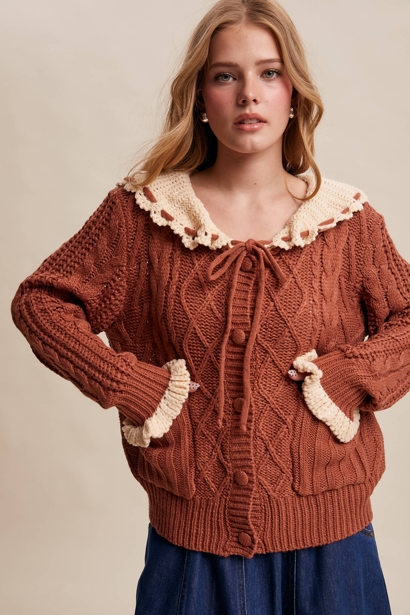 Woman wearing a brown knitted cardigan with lace trim on a beige background