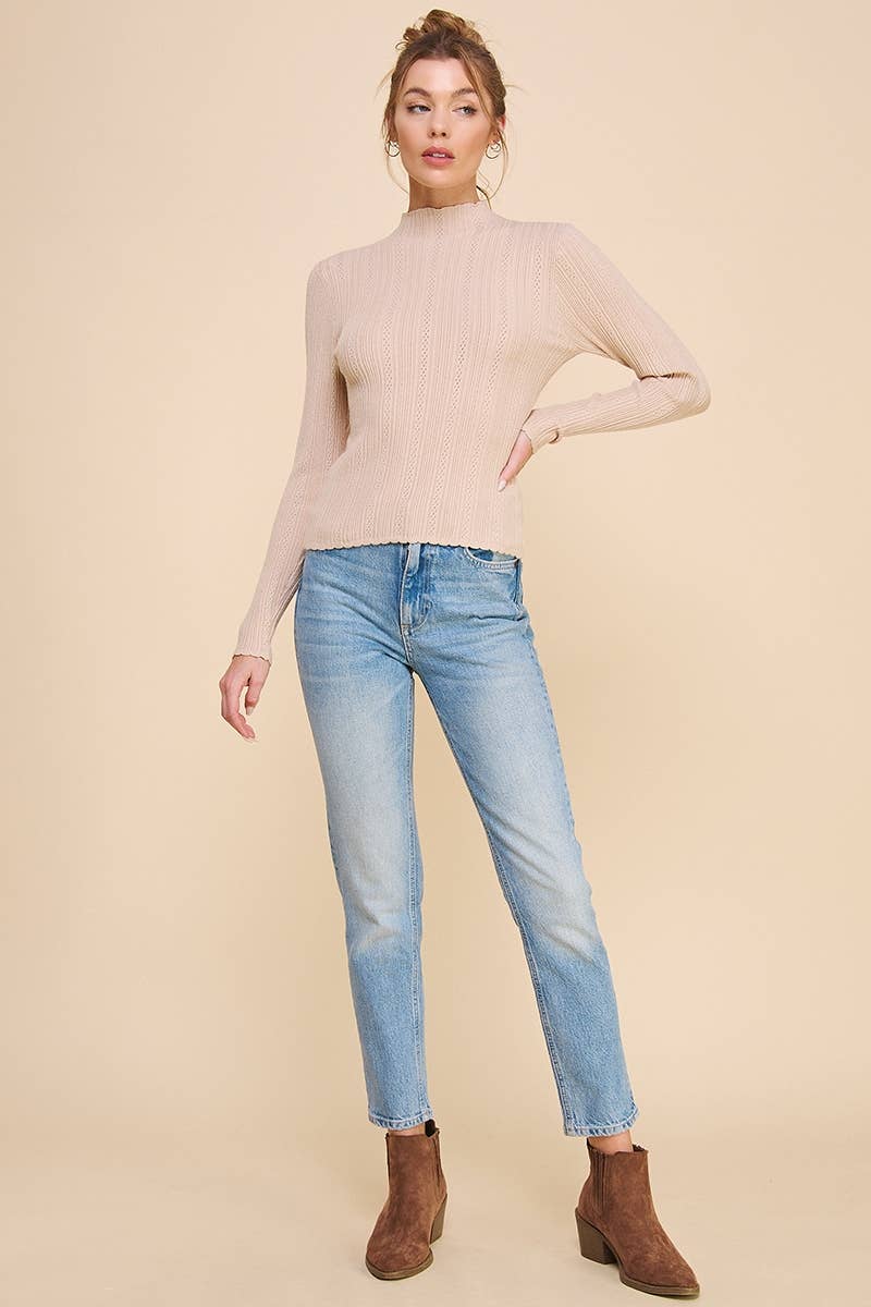 Woman wearing a beige sweater, light blue jeans, and brown boots on a beige background