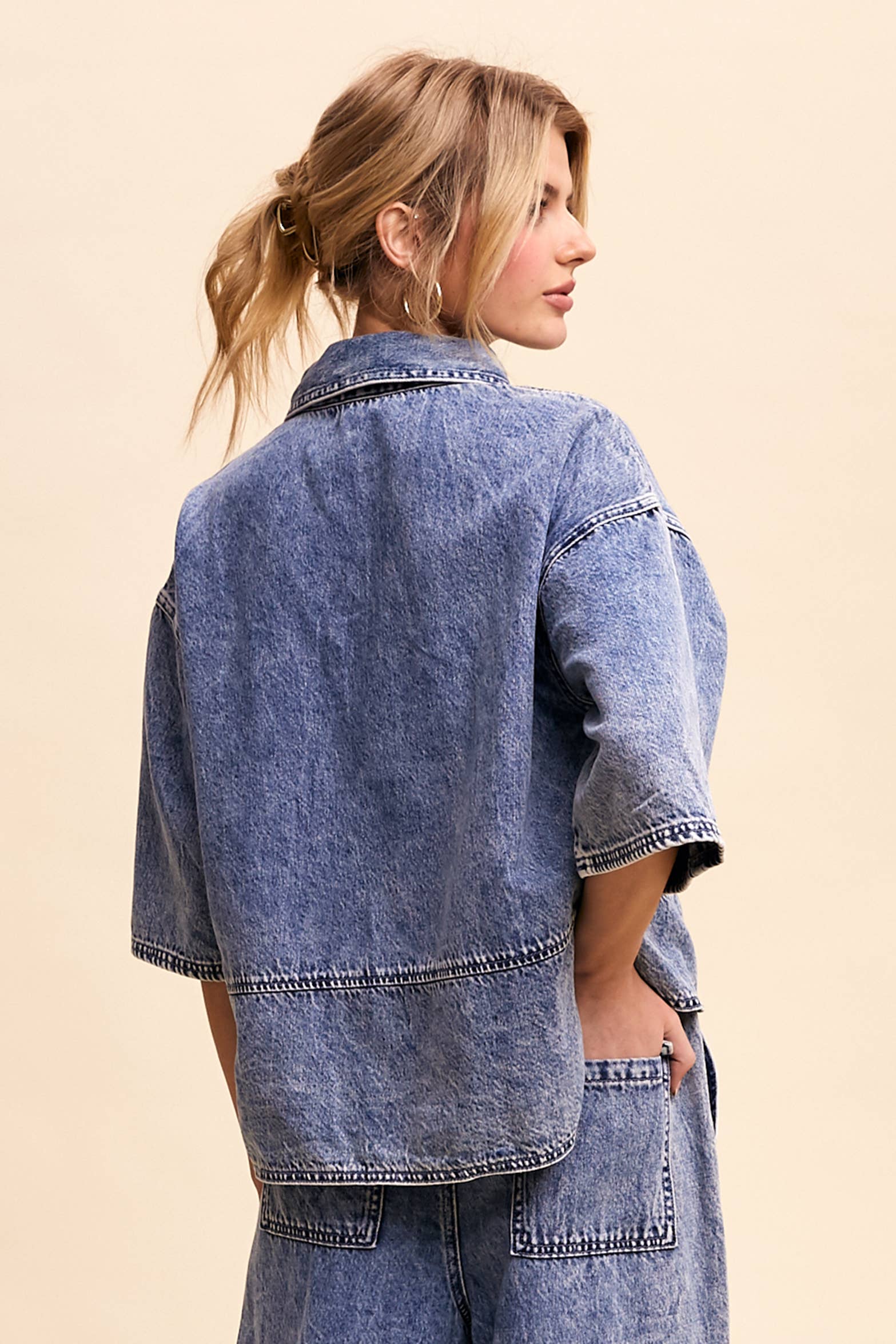 Back view- Light-wash denim pullover top with a half-button placket, exposed seam panels, and wide elbow-length sleeves in a relaxed, boxy fit.