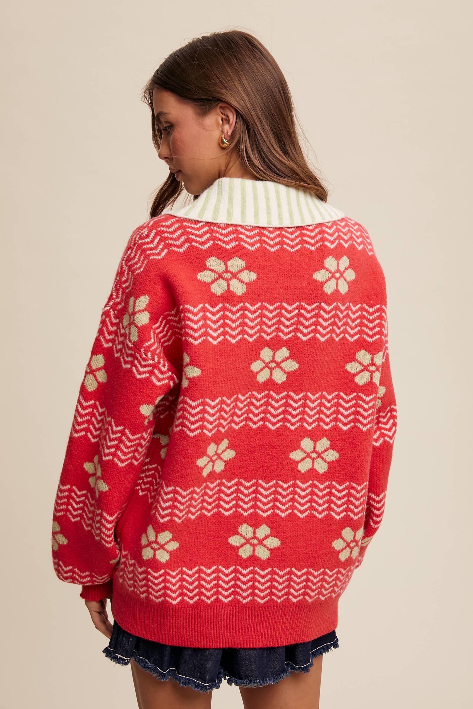 Red sweater with white patterns worn by a person on a beige background