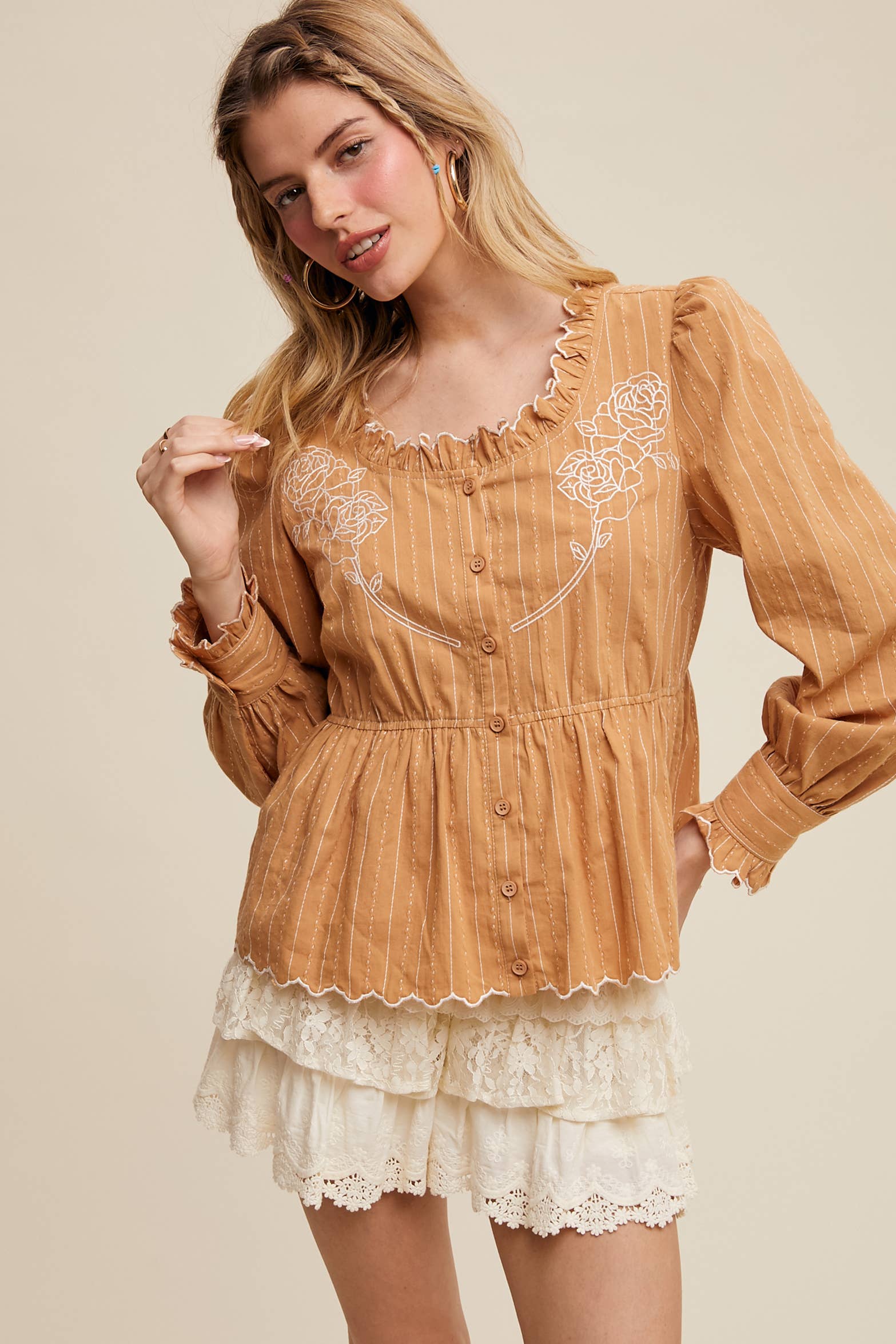 Camel pinstripe blouse with ruffled neckline, white rose embroidery, puff long sleeves, button front, and scalloped peplum hem—styled with white lace shorts.