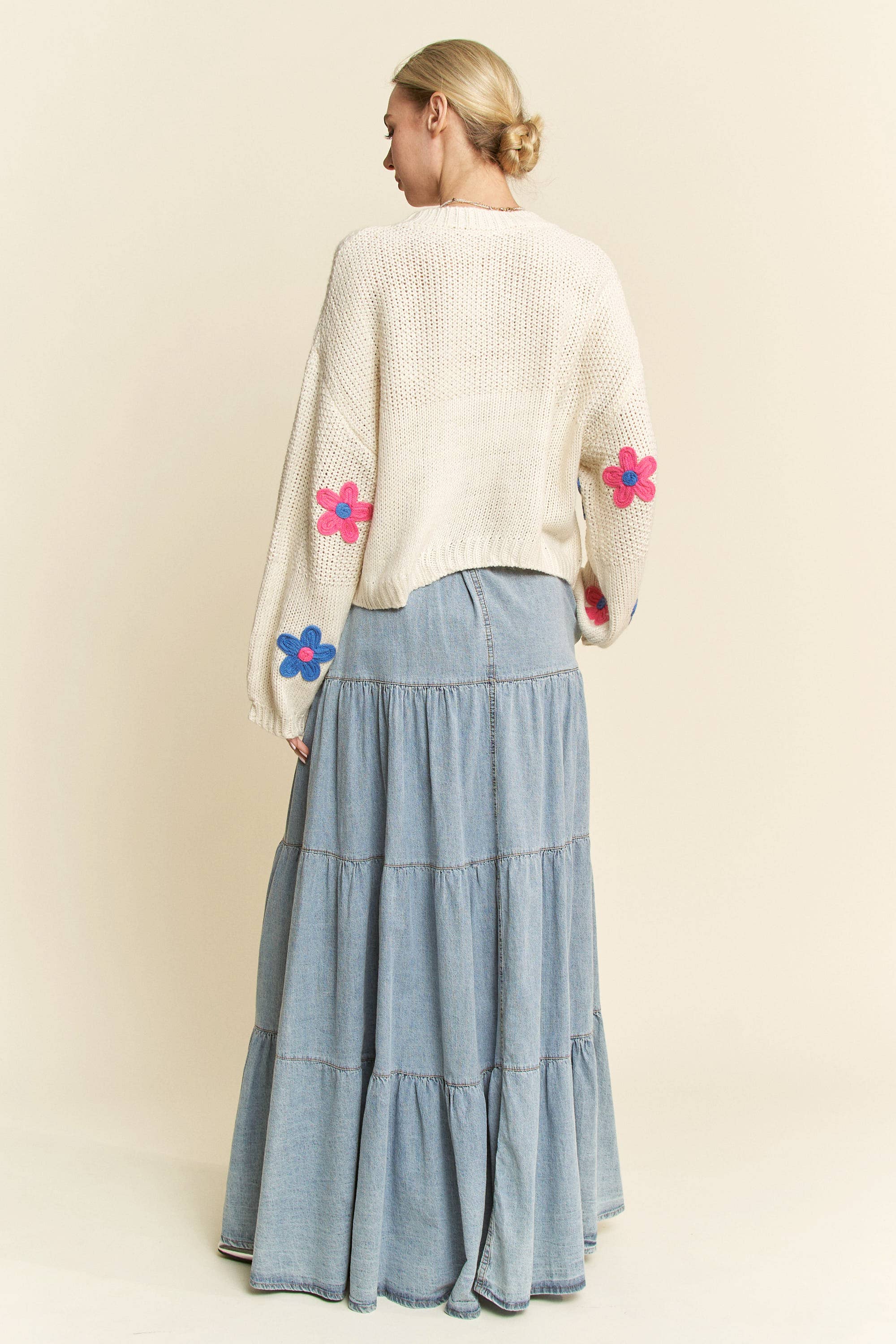 Back view- Cream knit sweater with colorful 3D floral appliqués in pink, blue, and green, styled with a button-front light denim skirt.