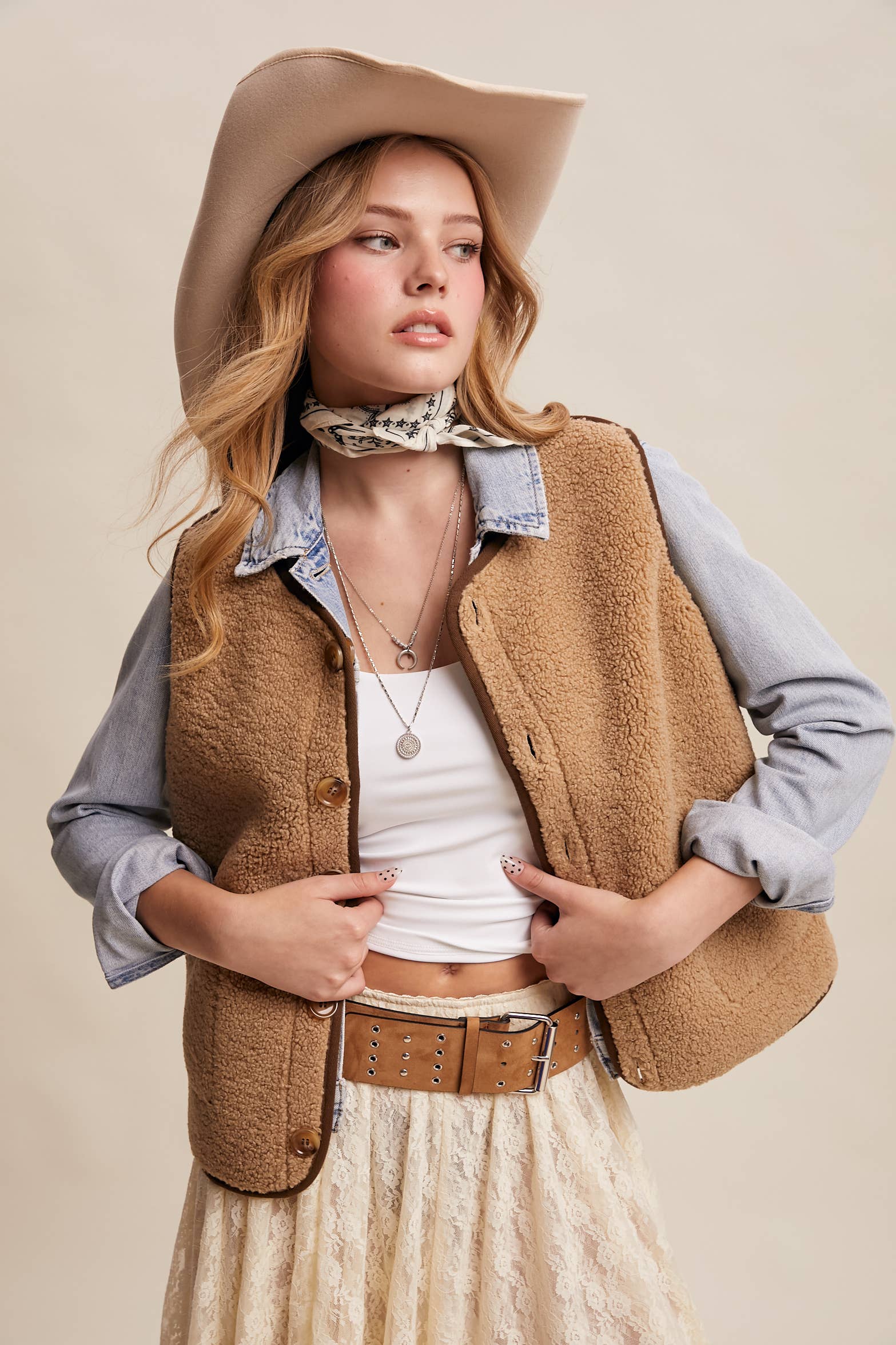 Woman wearing a tan vest, white shirt, and beige hat on a beige background