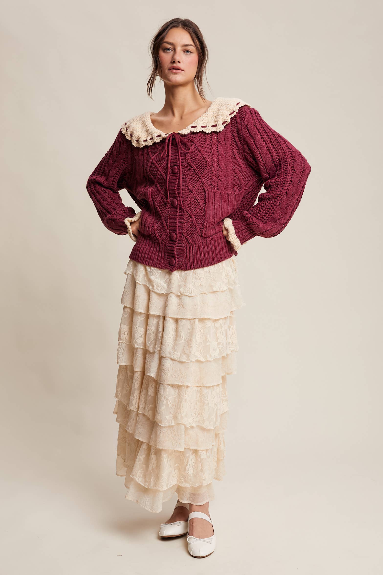 Woman wearing a burgundy sweater with lace trim and a beige layered skirt on a plain background