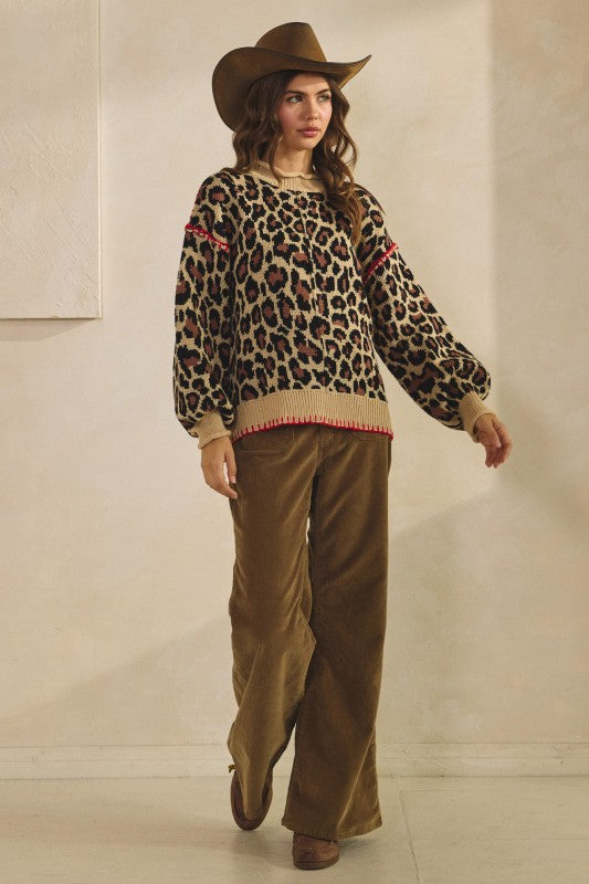 Leopard print knit sweater in tan with ribbed crew neck, cuffs and hem and red whipstitch trim, styled with brown corduroy pants and a cowboy hat.