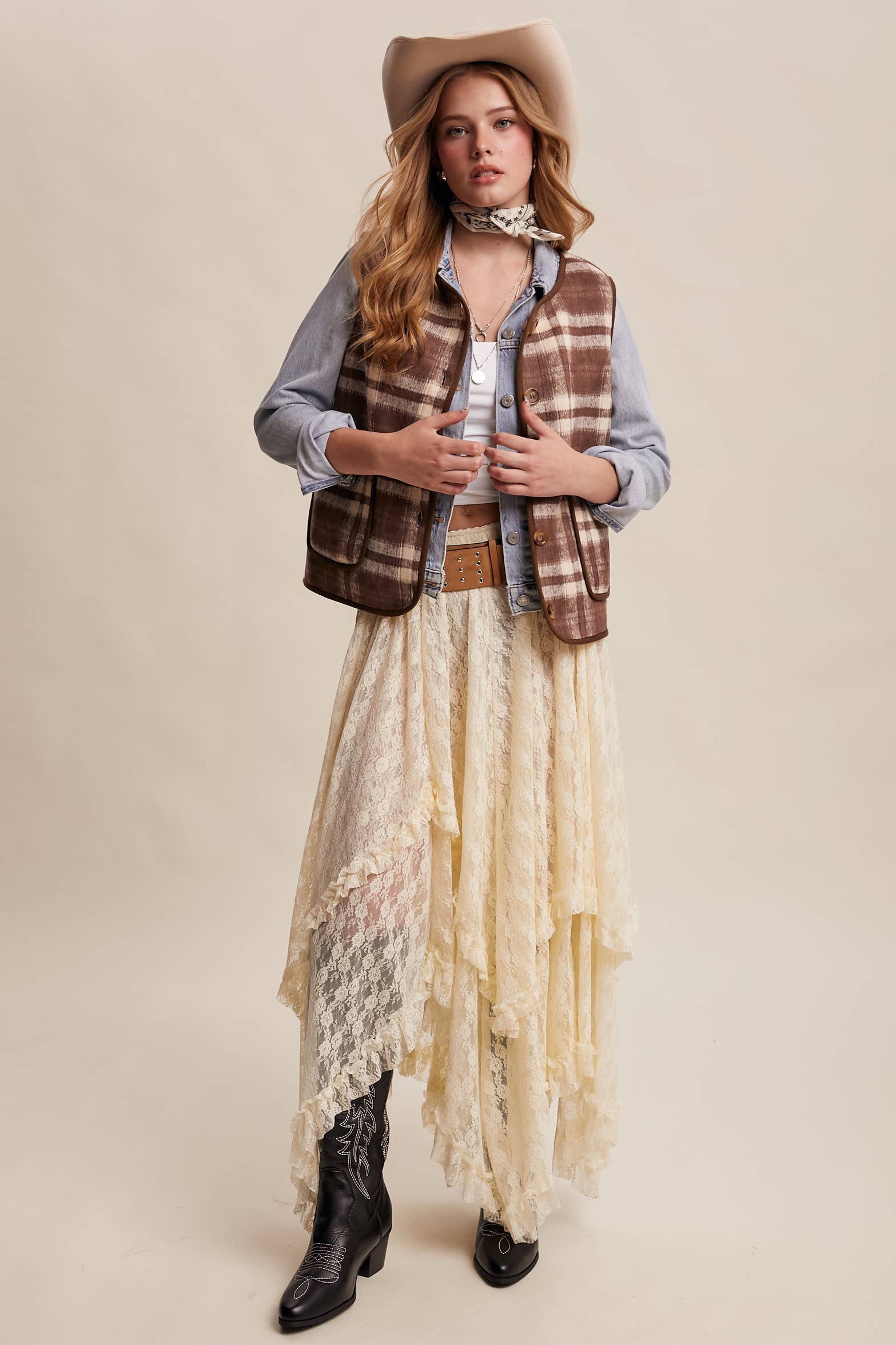 Woman wearing a plaid vest, lace dress, and cowboy hat on a beige background