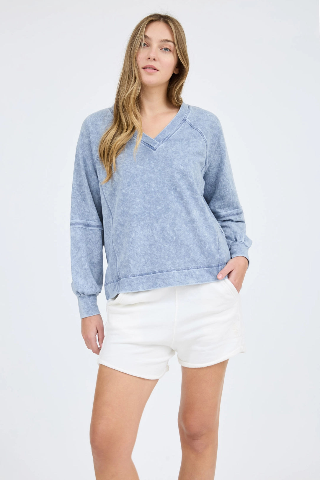 Woman wearing a blue sweater and white shorts on a light gray background