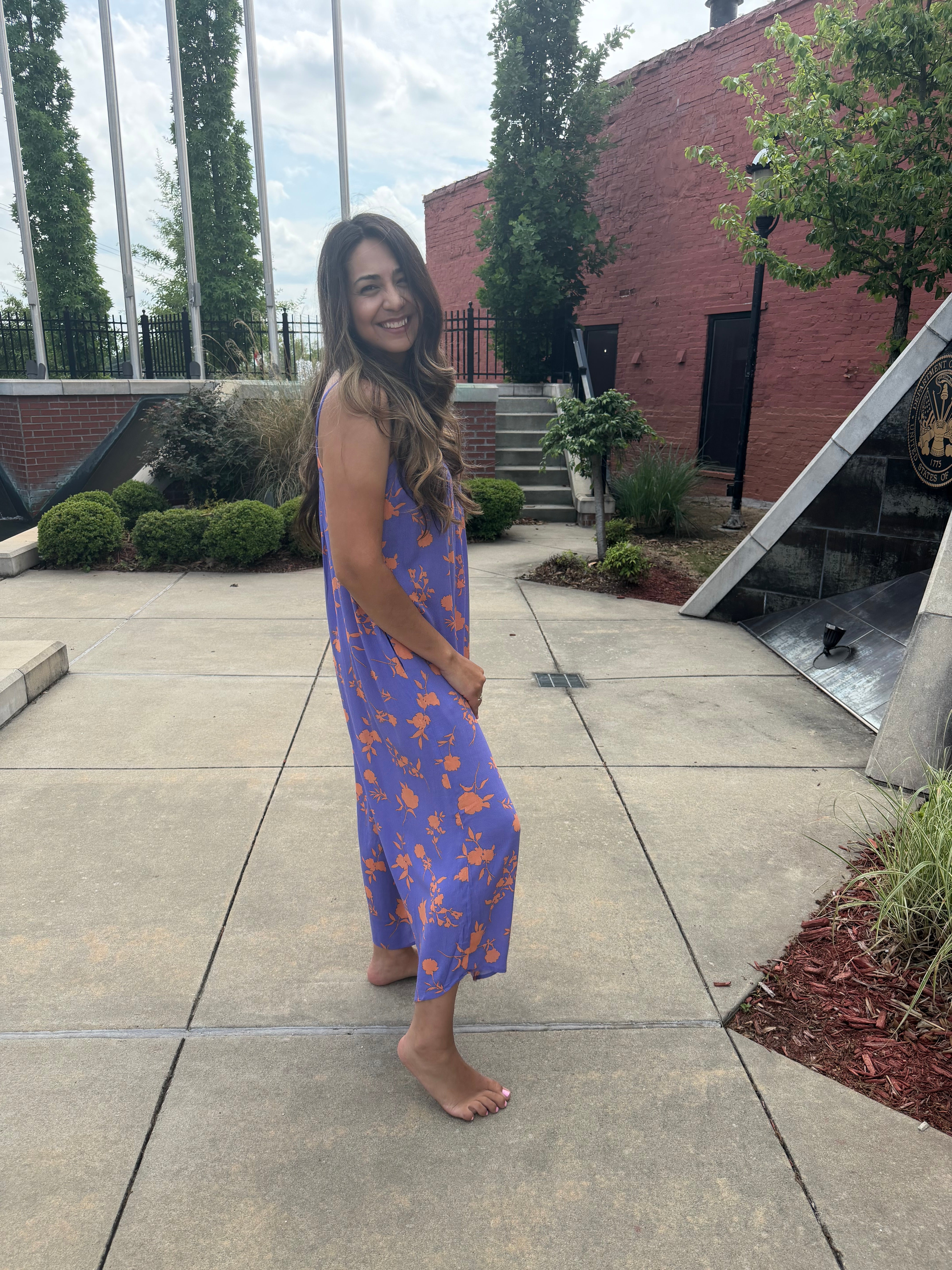 Woman in a blue floral dress standing on a sidewalk with trees and buildings in the background