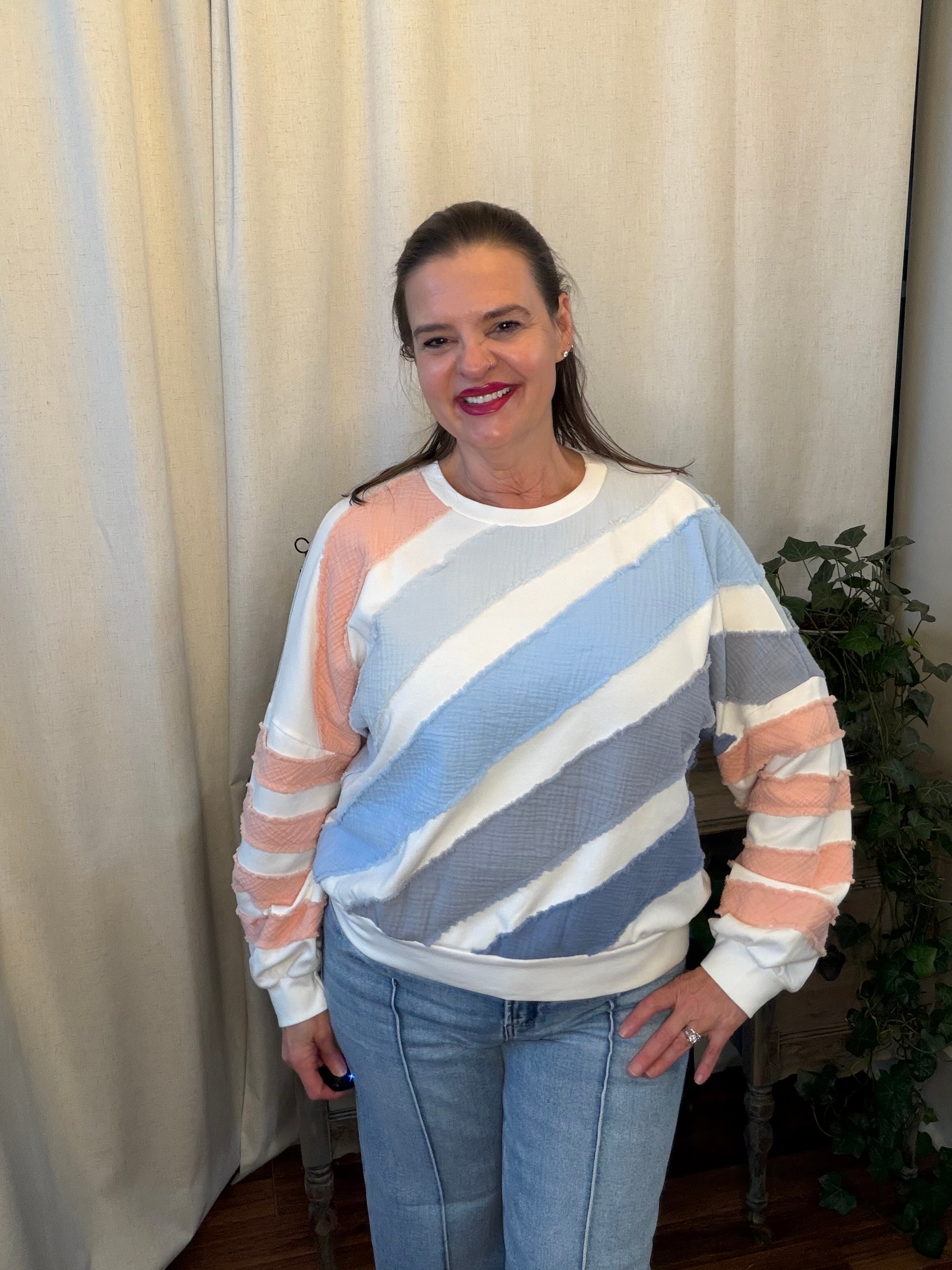Woman wearing a striped sweater and jeans standing against a white curtain.