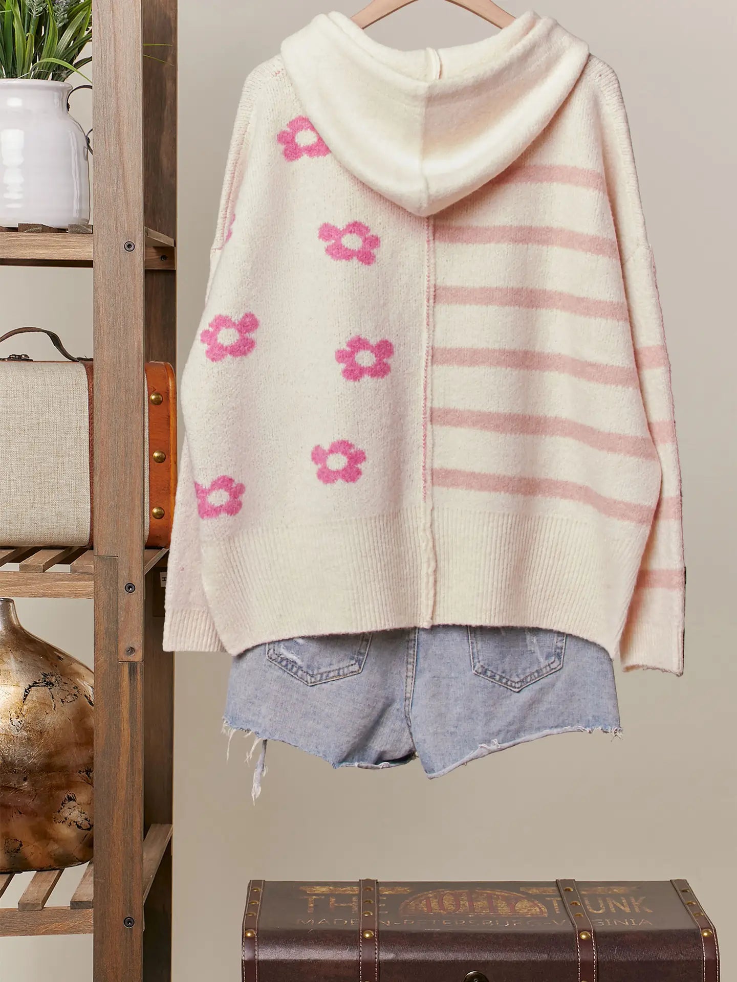 White cardigan with pink floral patterns and stripes, worn over denim shorts, on a wooden shelf.