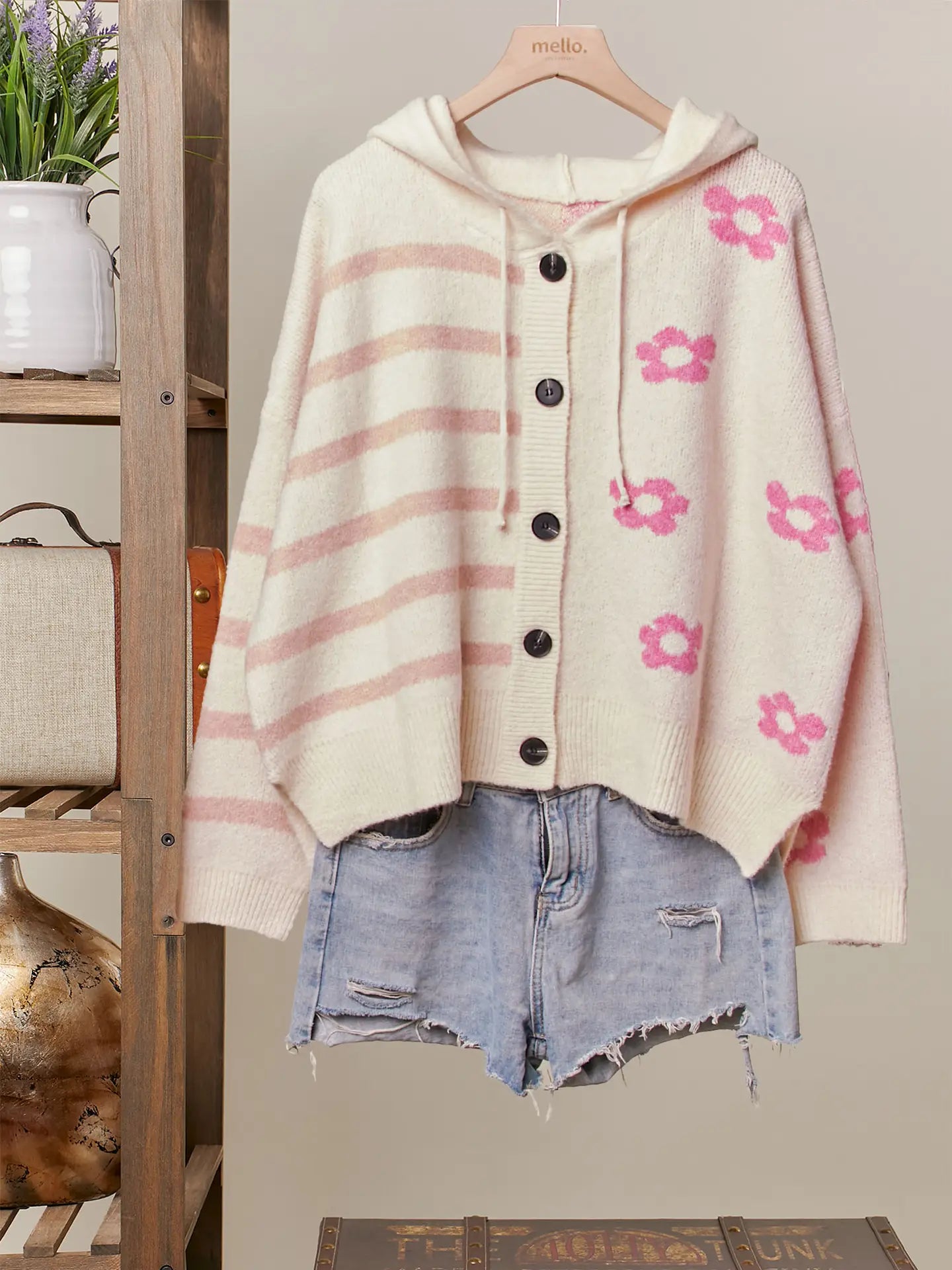 Beige cardigan with pink floral patterns and stripes, paired with denim shorts, on a wooden hanger against a neutral background.