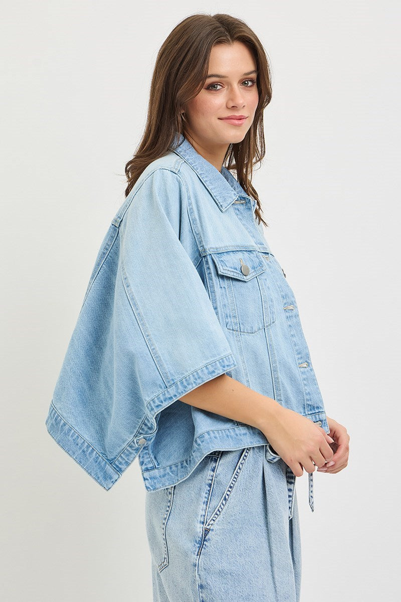 Woman wearing a light blue denim jacket and jeans on a plain background