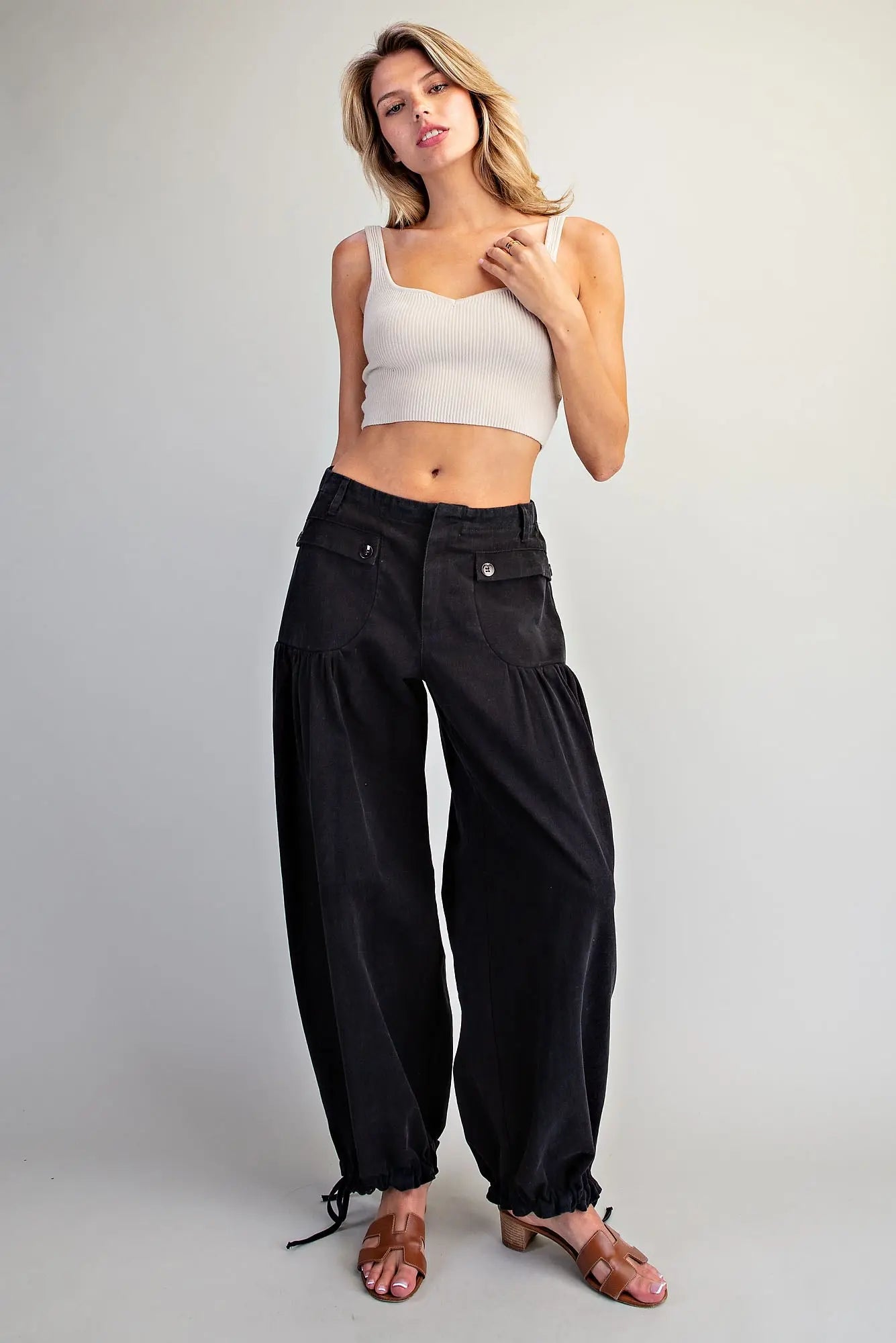 A woman modeling black wide-leg cropped pants with a white ribbed crop top and brown sandals, standing against a light gray studio background.
