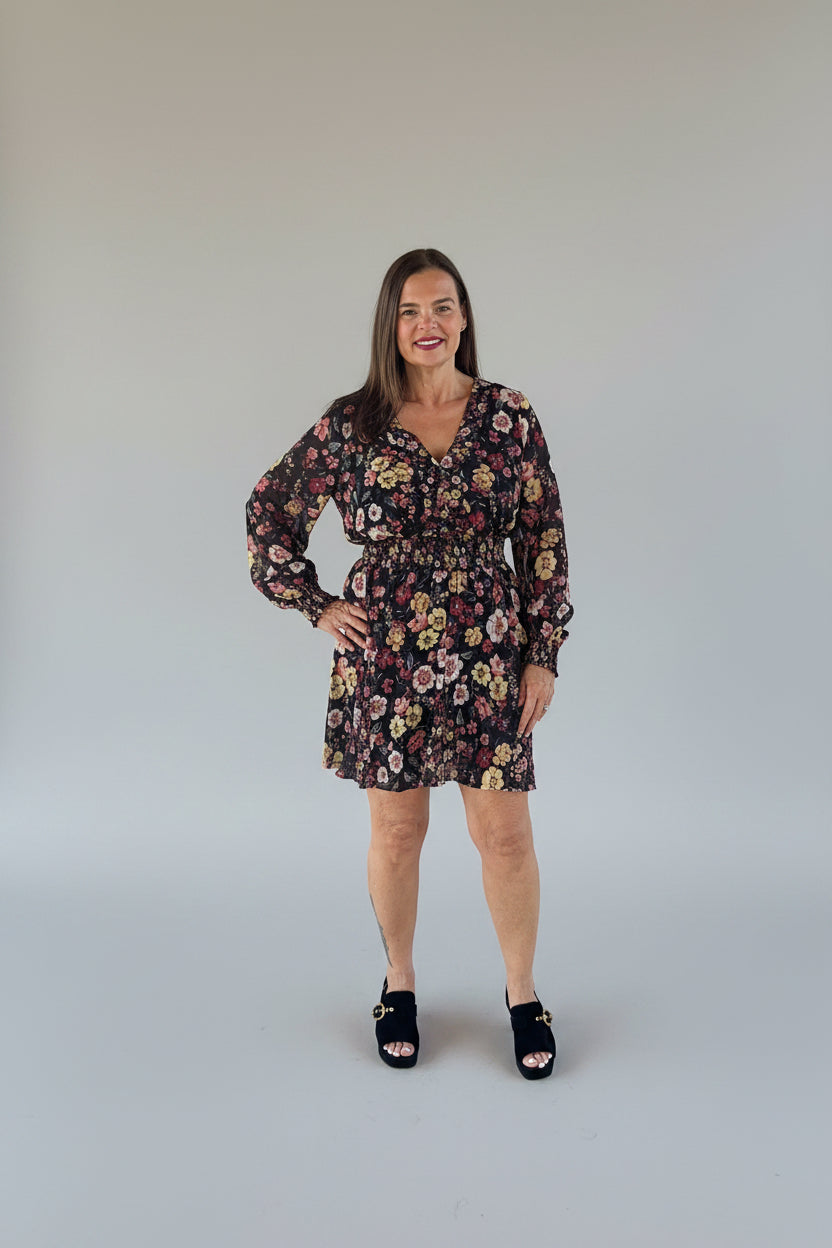 A woman modeling a black long-sleeve mini dress with a colorful floral print.