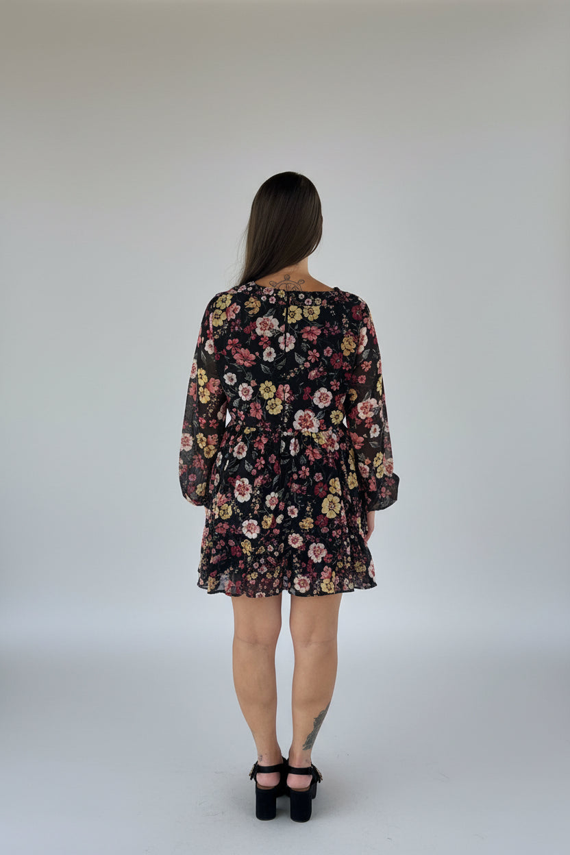 Woman in Smocked Waist V-Neck Mini Dress in black multicolor floral print, back view showing long smocked cuffs and pleated mini skirt, styled with black platform heels