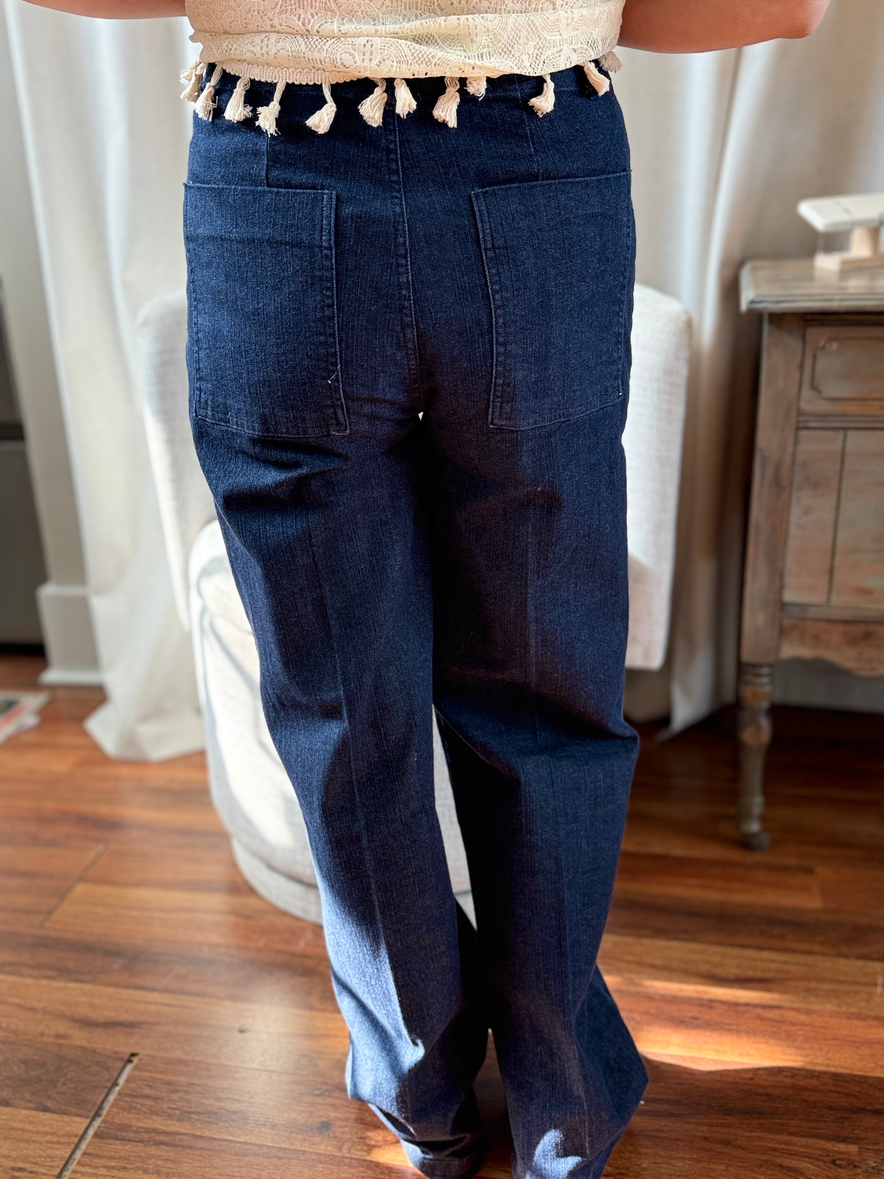 Person wearing blue jeans in a room with wooden floor and white curtains.
