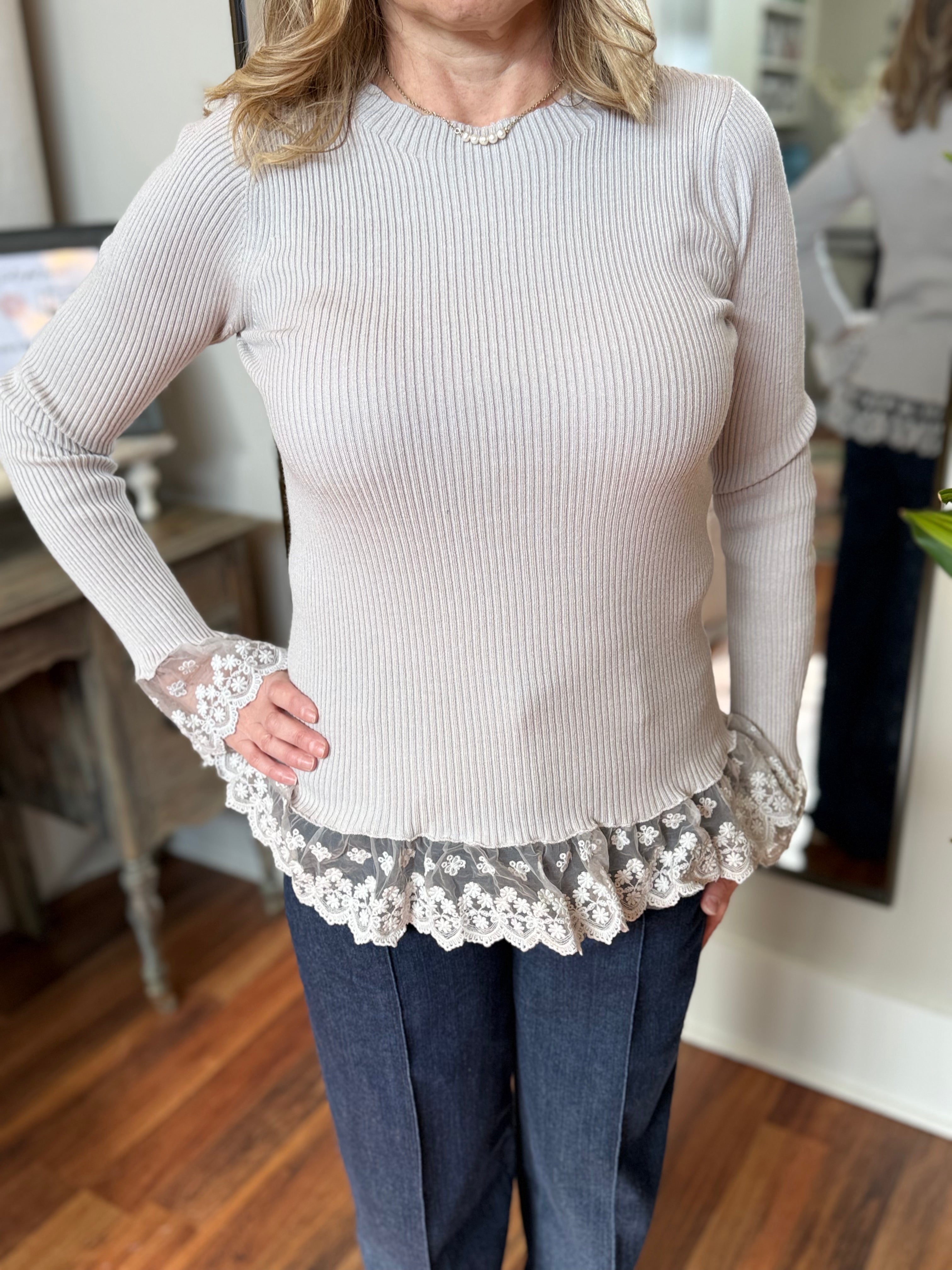 Woman wearing a light pink sweater with lace cuffs in an indoor setting