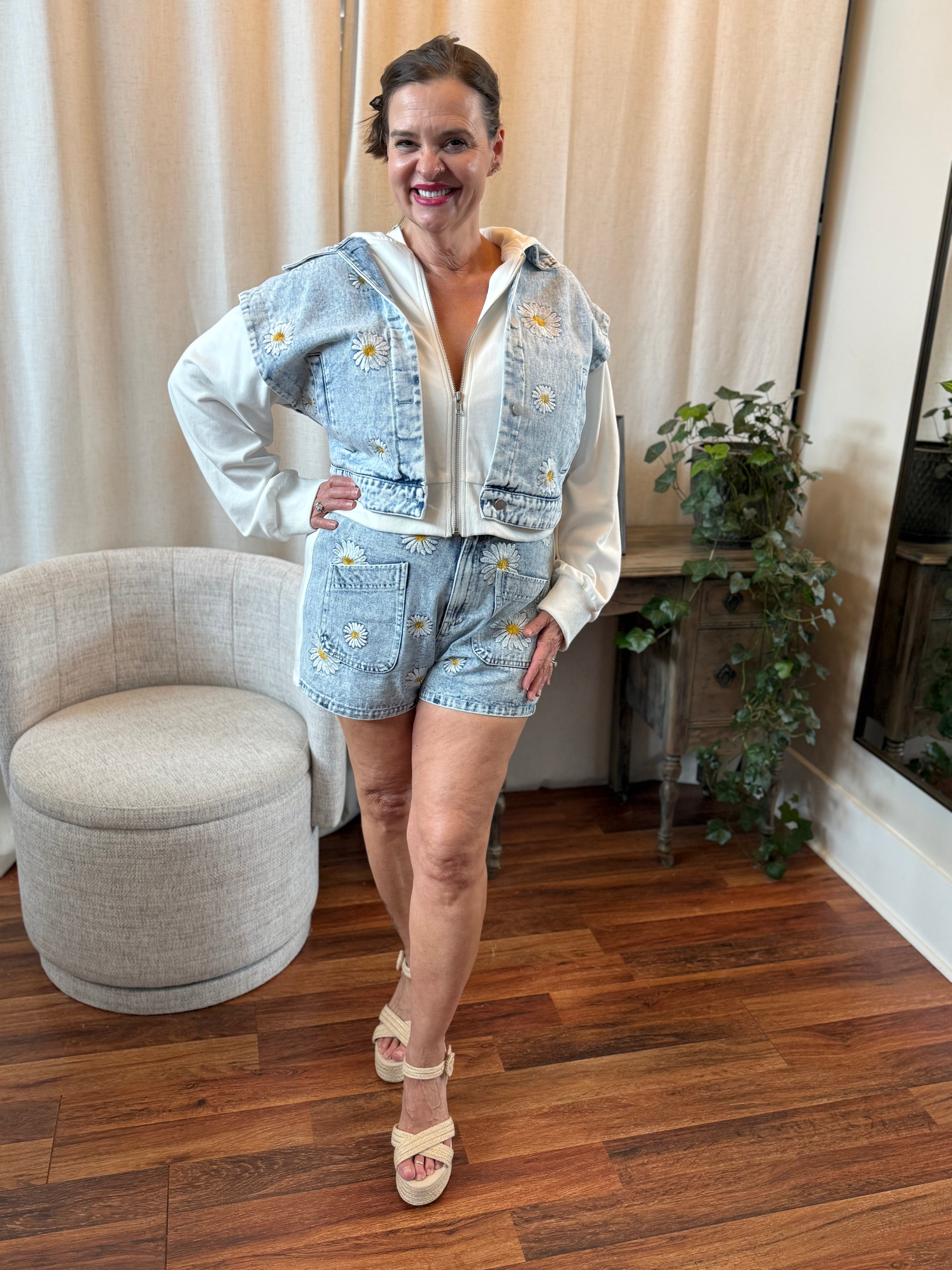 Woman in denim outfit standing in a room with wooden floor and beige curtains.