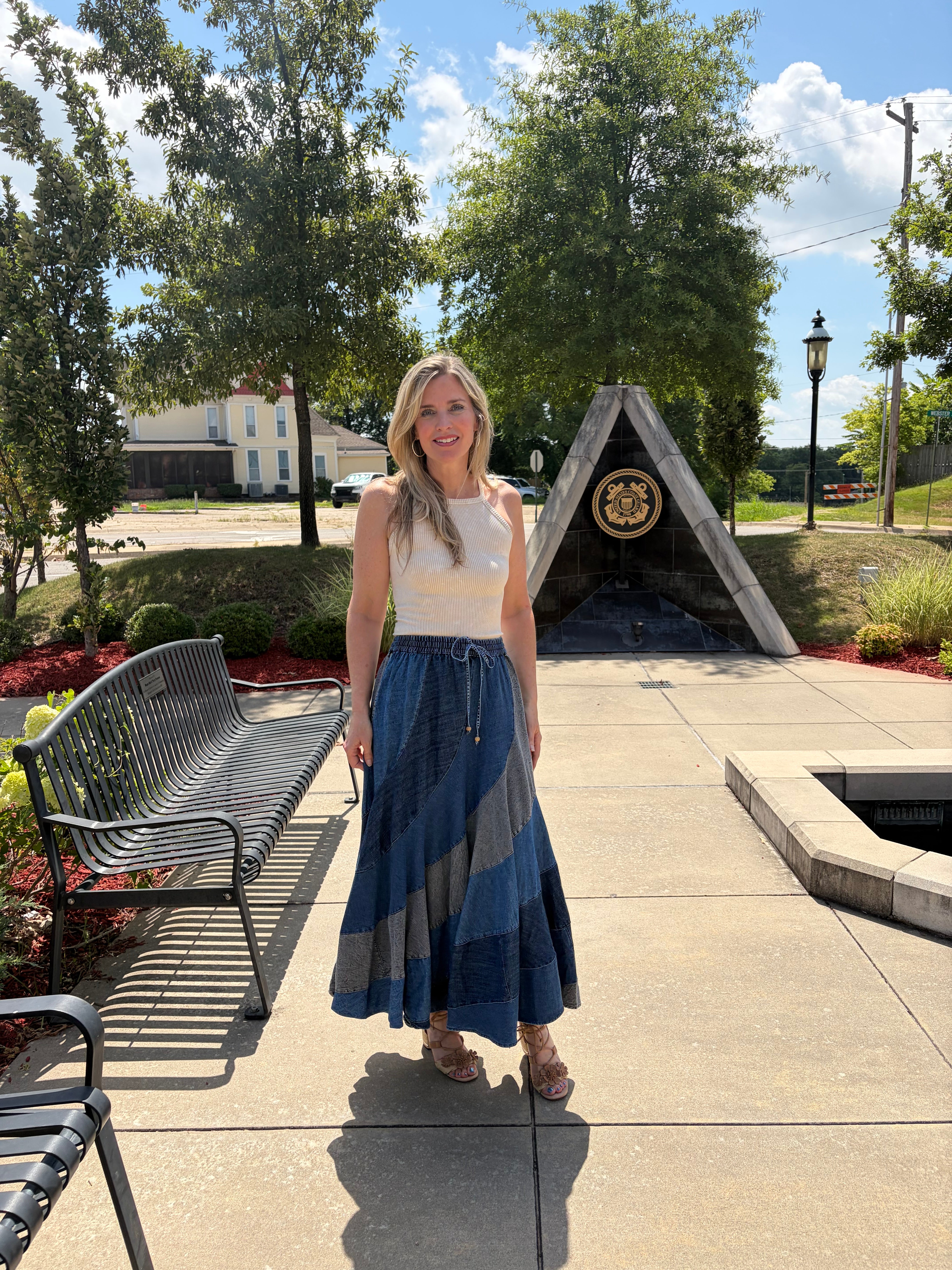Front full-body shot, model facing camera in patchwork denim bias skirt with drawstring waist, white tank top, sandals, outdoor setting