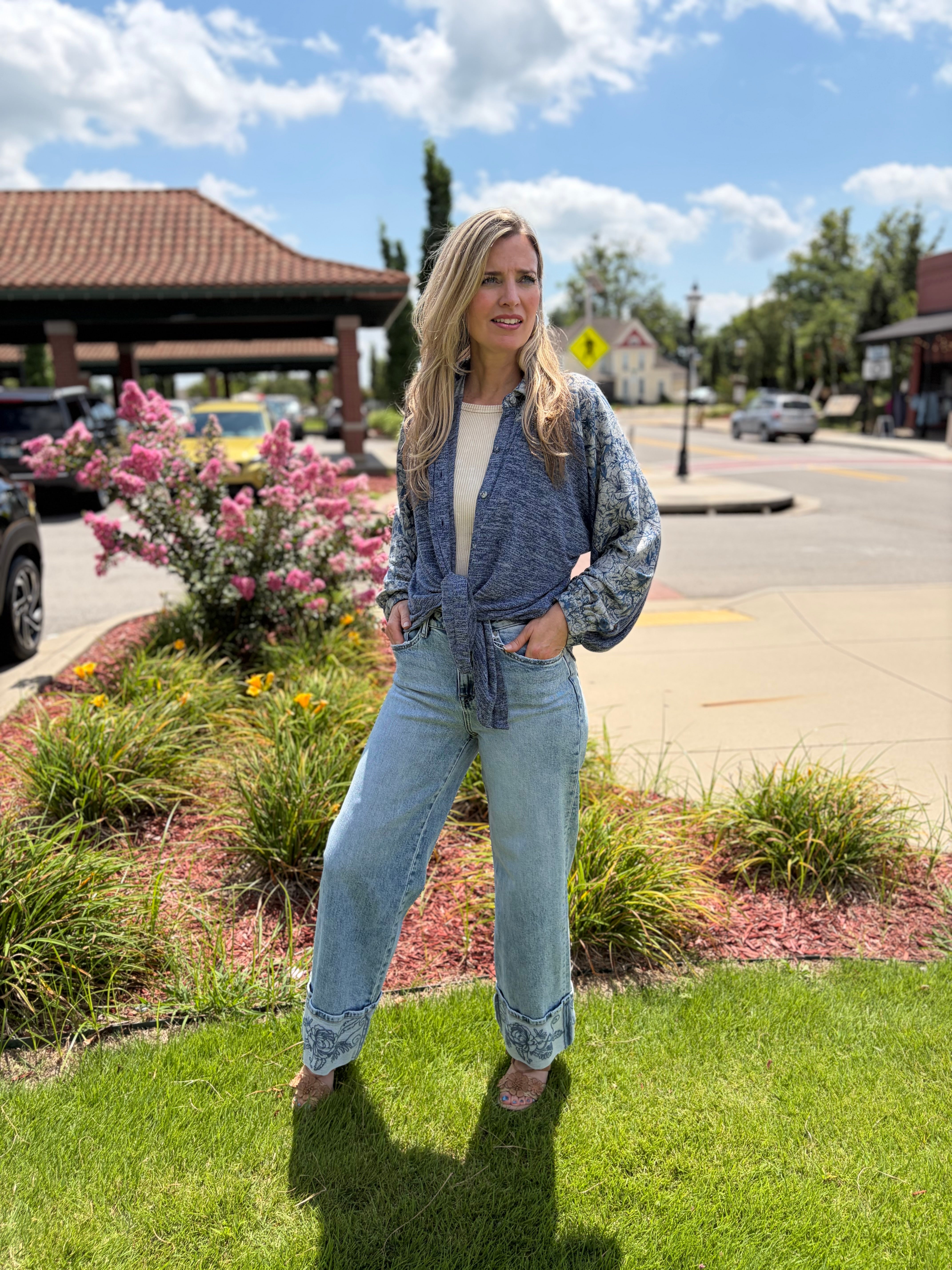 Woman wearing blue bohemian sweater knit shirt tied at waist with floral print balloon sleeves, styled with light wash wide-leg jeans