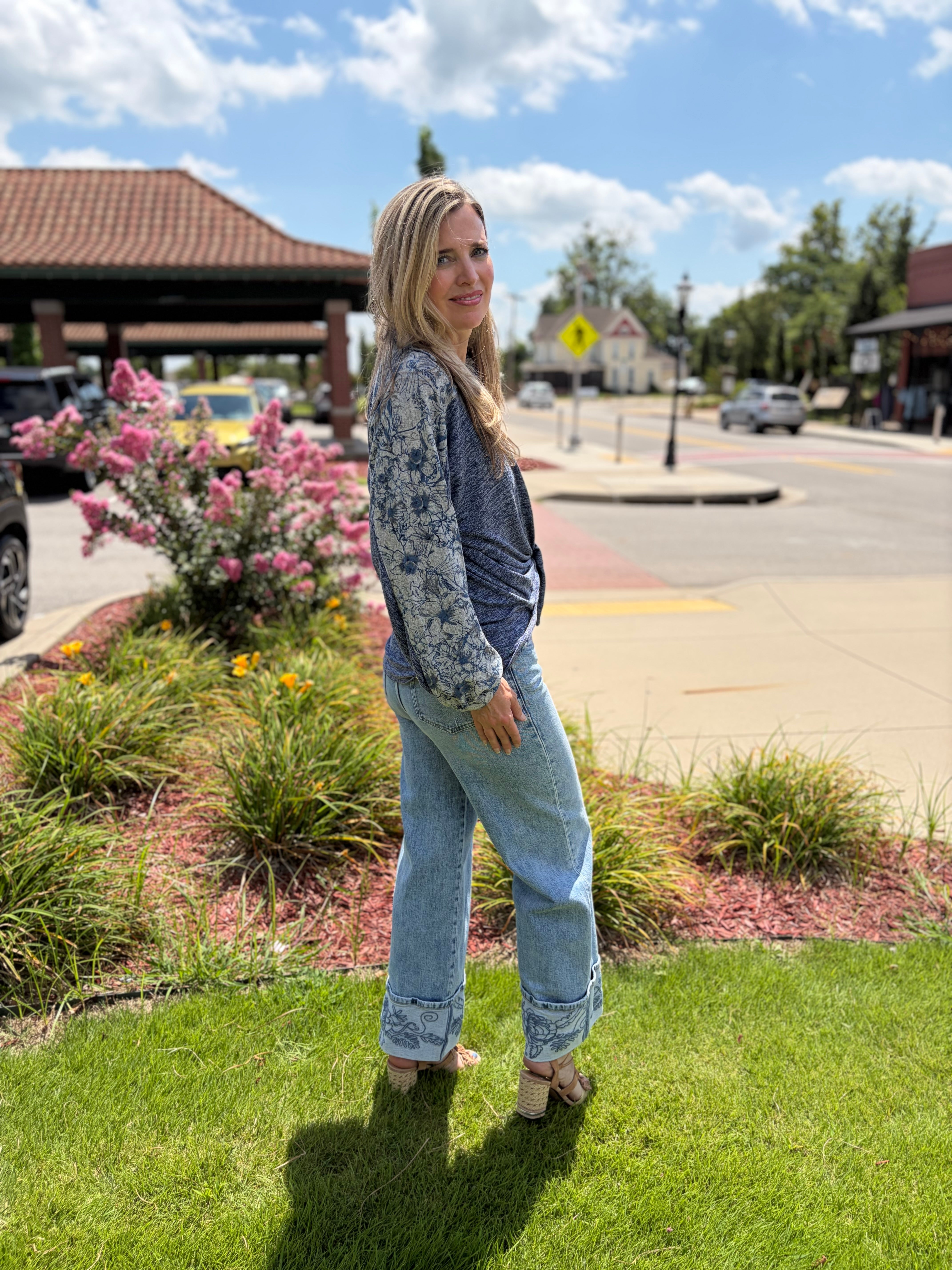 Side view of model in blue boho sweater knit shirt with floral balloon sleeves tied at waist over wide-leg jeans