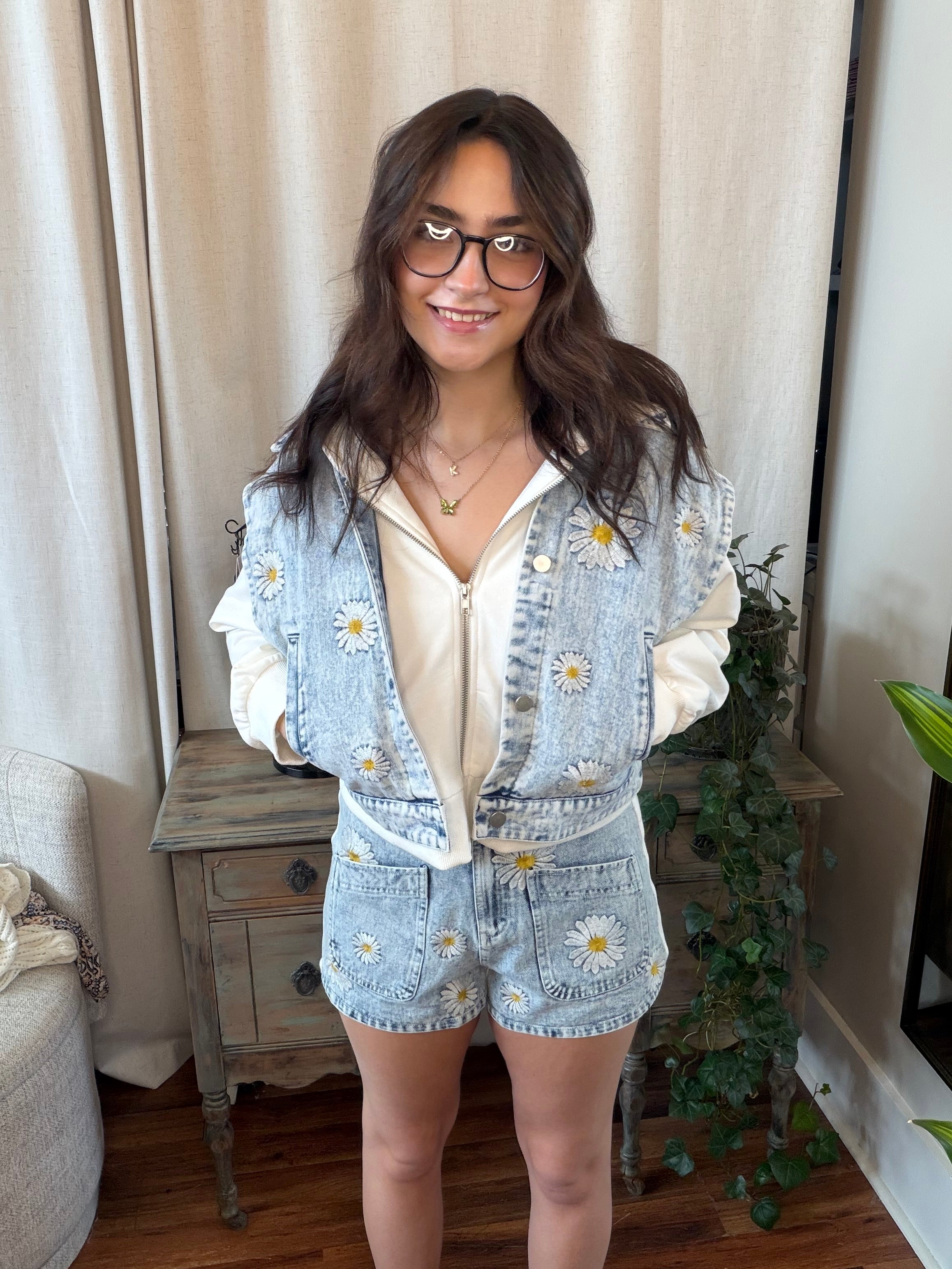 Woman wearing a light blue floral outfit indoors with curtains and a plant in the background
