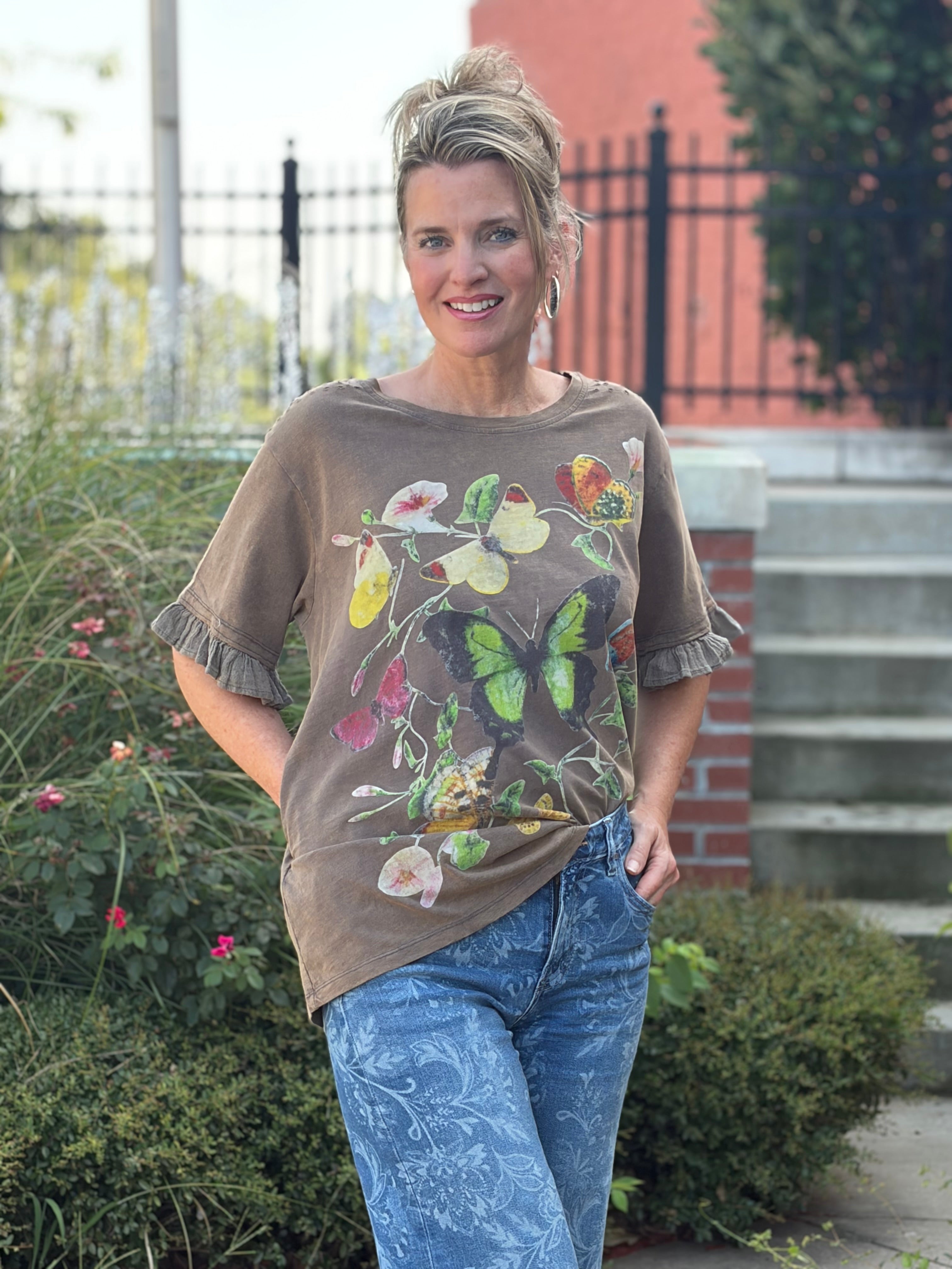 mocha brown botanical butterfly graphic, ruffle sleeve trim, green butterfly print, styled with floral jeans outdoors