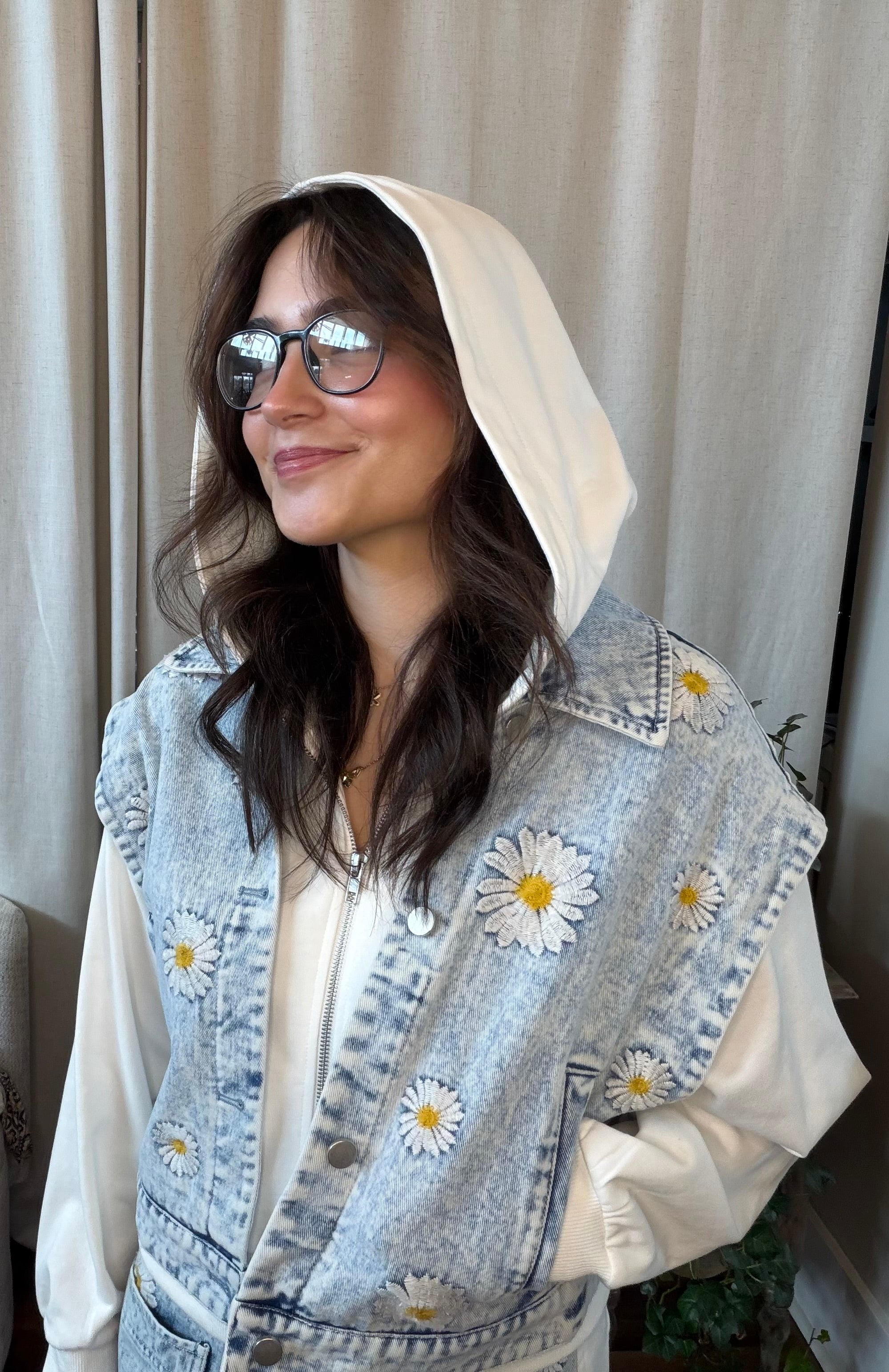 Person wearing a denim vest with floral embroidery against a neutral background