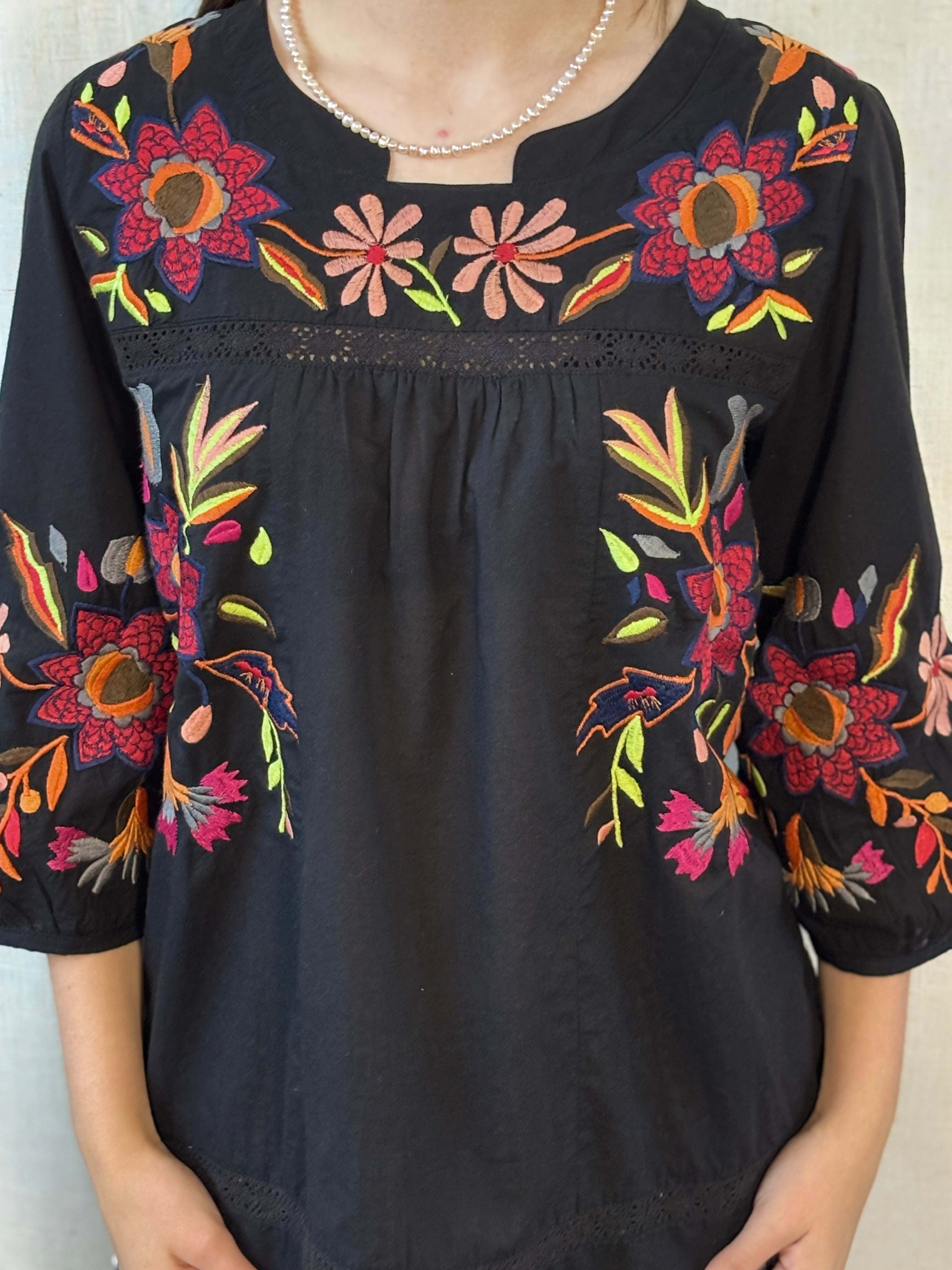 Close-up of hand embroidery on Anü Vibrant Floral Embroidered Blouse — multicolor florals in pink, orange, red, and green on black cotton with lace trim neckline