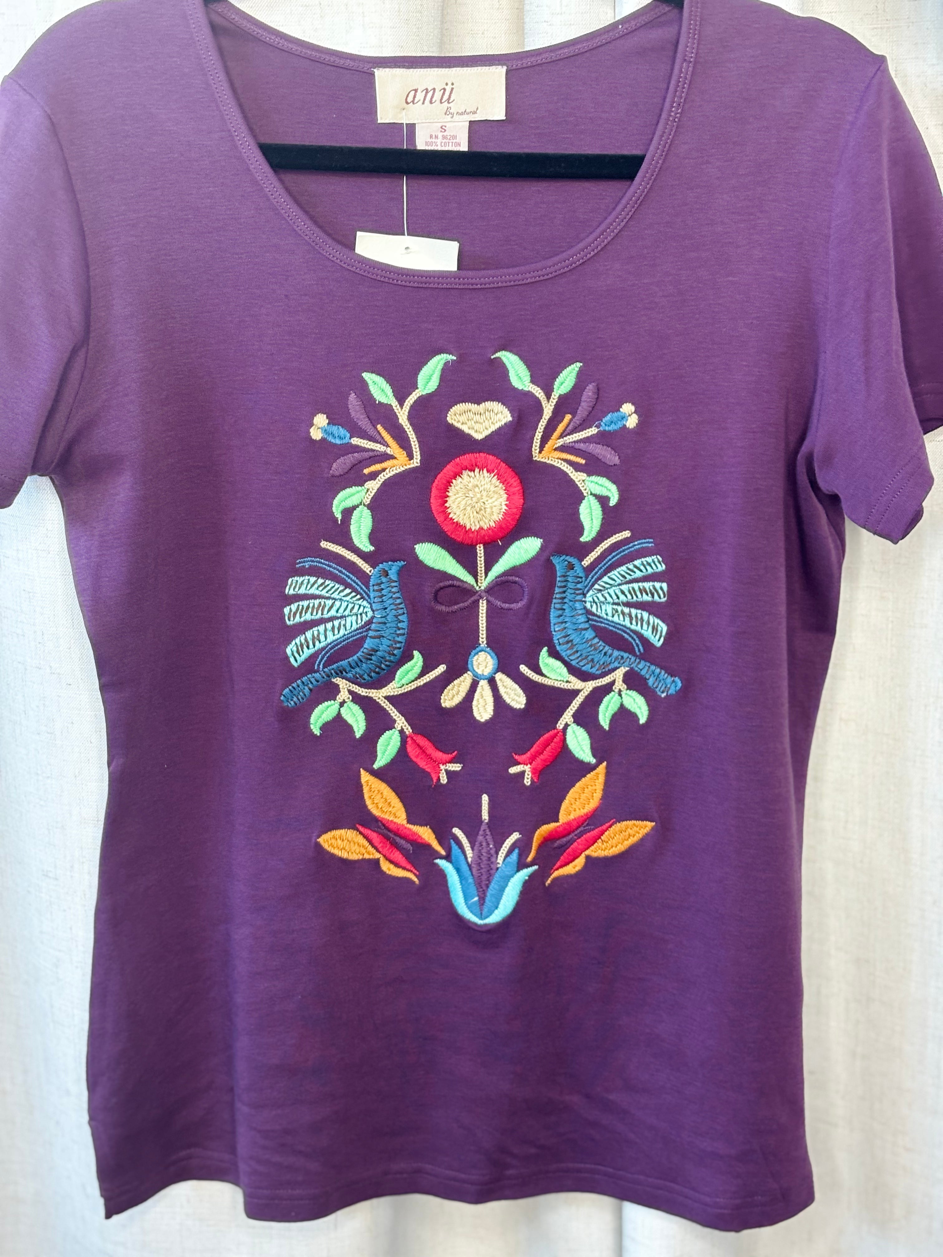 Close-up of hand embroidery detail on Anü Birds & Butterflies Tee — folk-art birds, florals, and botanical motifs in multicolor thread
