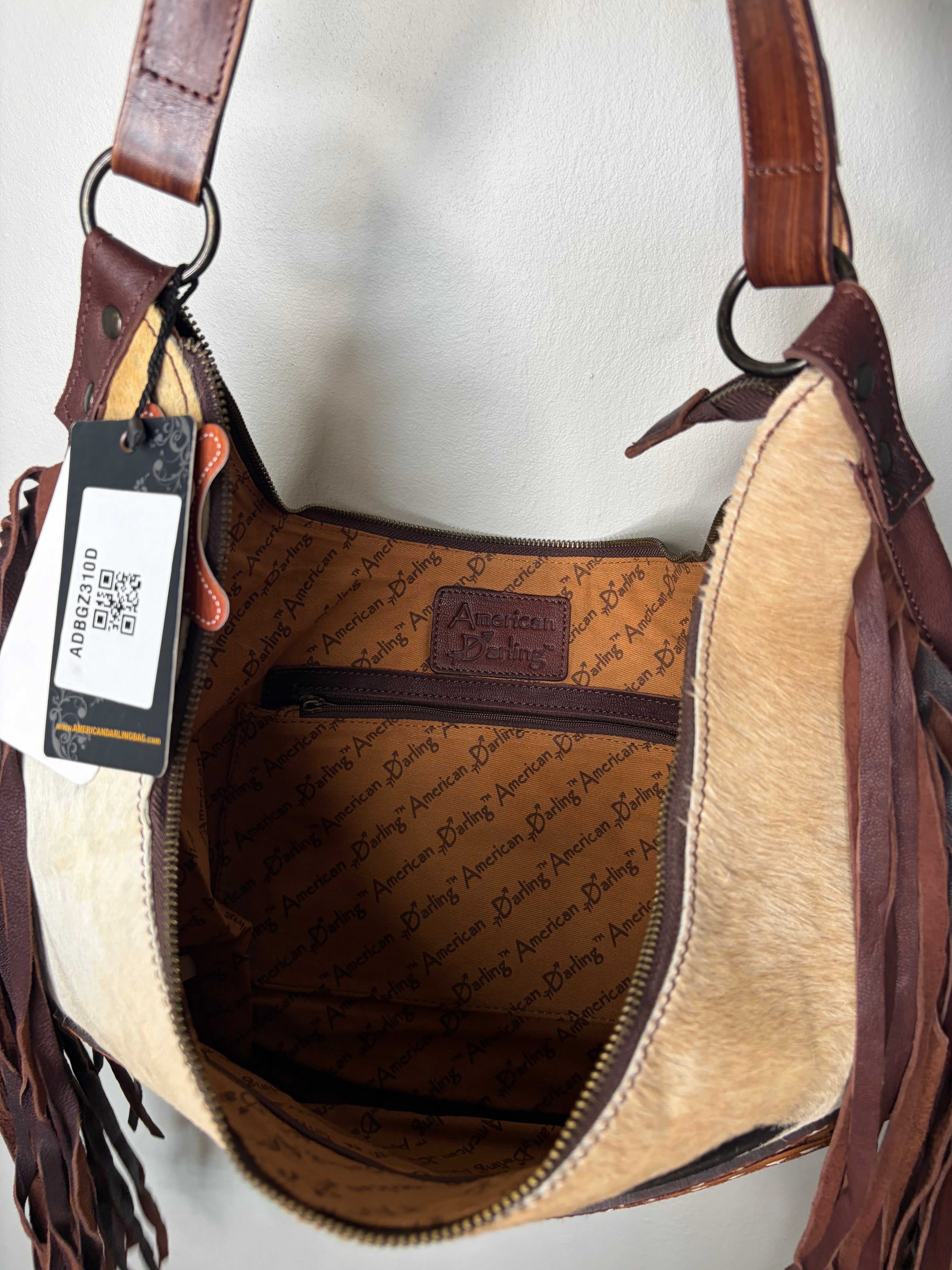 A close-up of a handbag's interior showing tan and brown cowhide and leather trim, with a hanging product tag attached on the left side.