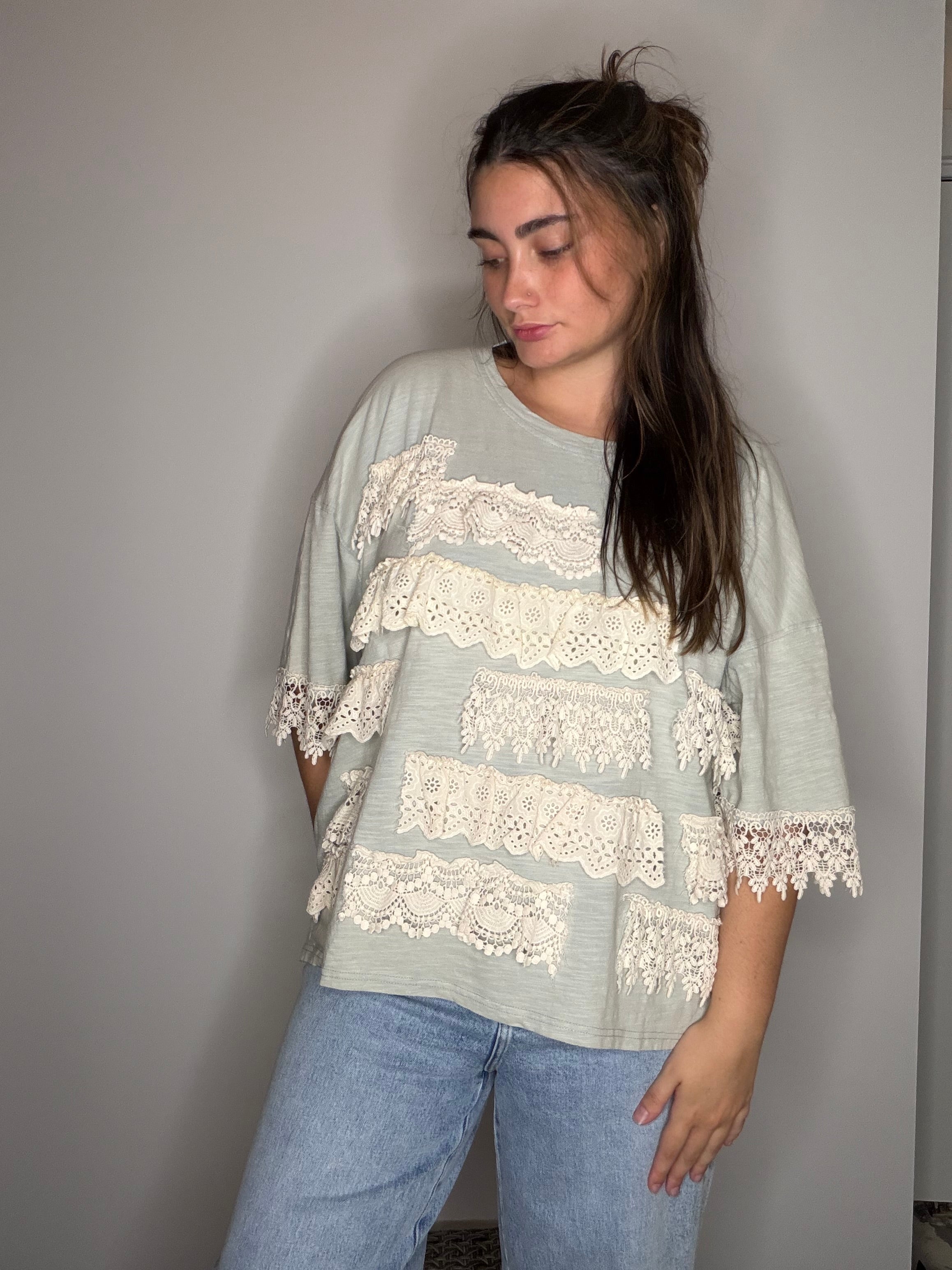 Side-glance front view: sage green top with tiered cream crochet lace ruffles, paired with jeans