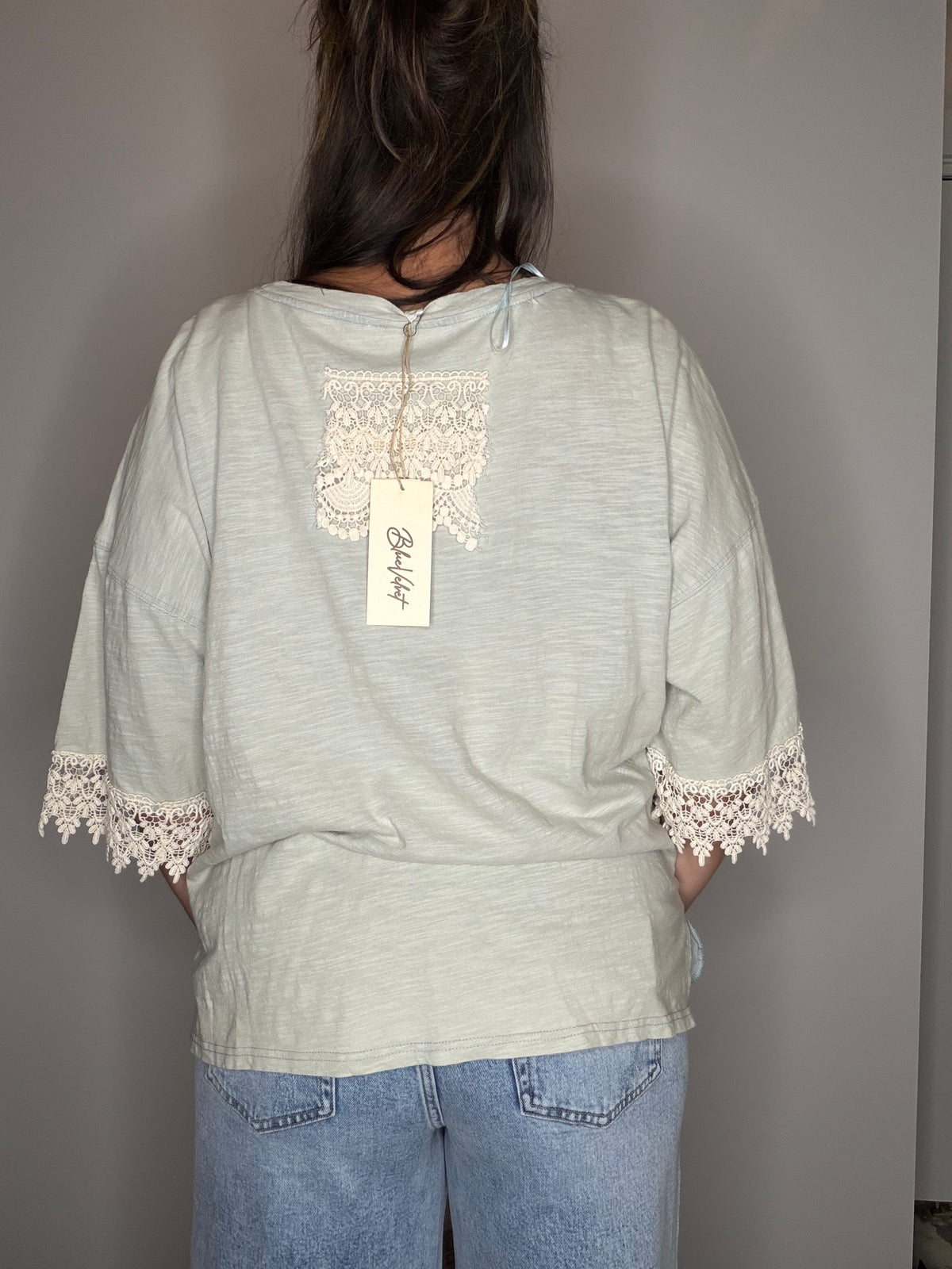 Back view: lace back detail, trimmed sleeves, and brand hangtag visible