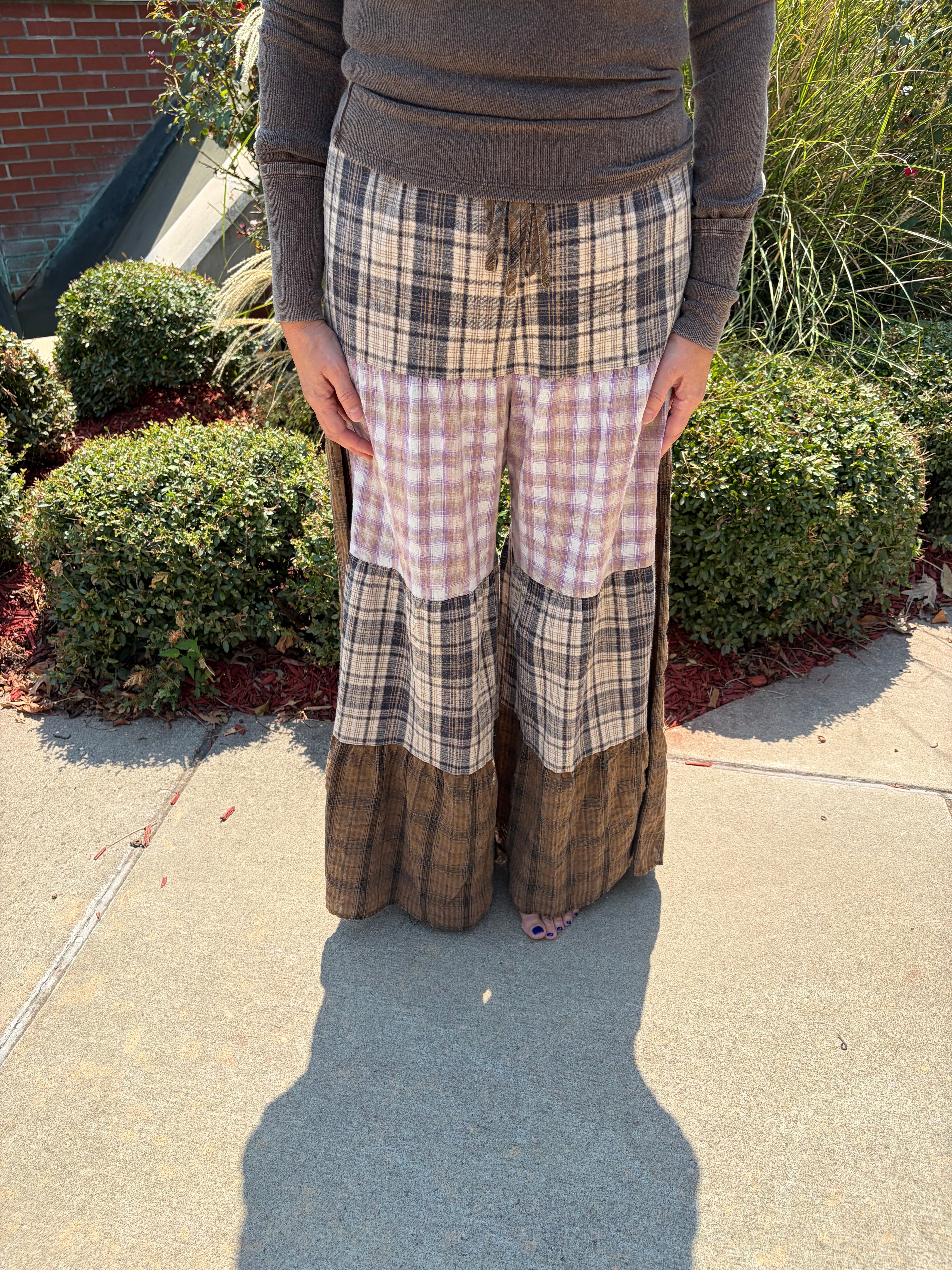 Close-up front view of Patchwork Plaid Maxi Pants showing tiered patchwork plaid panels in dark brown, blush, and taupe with drawstring waistband