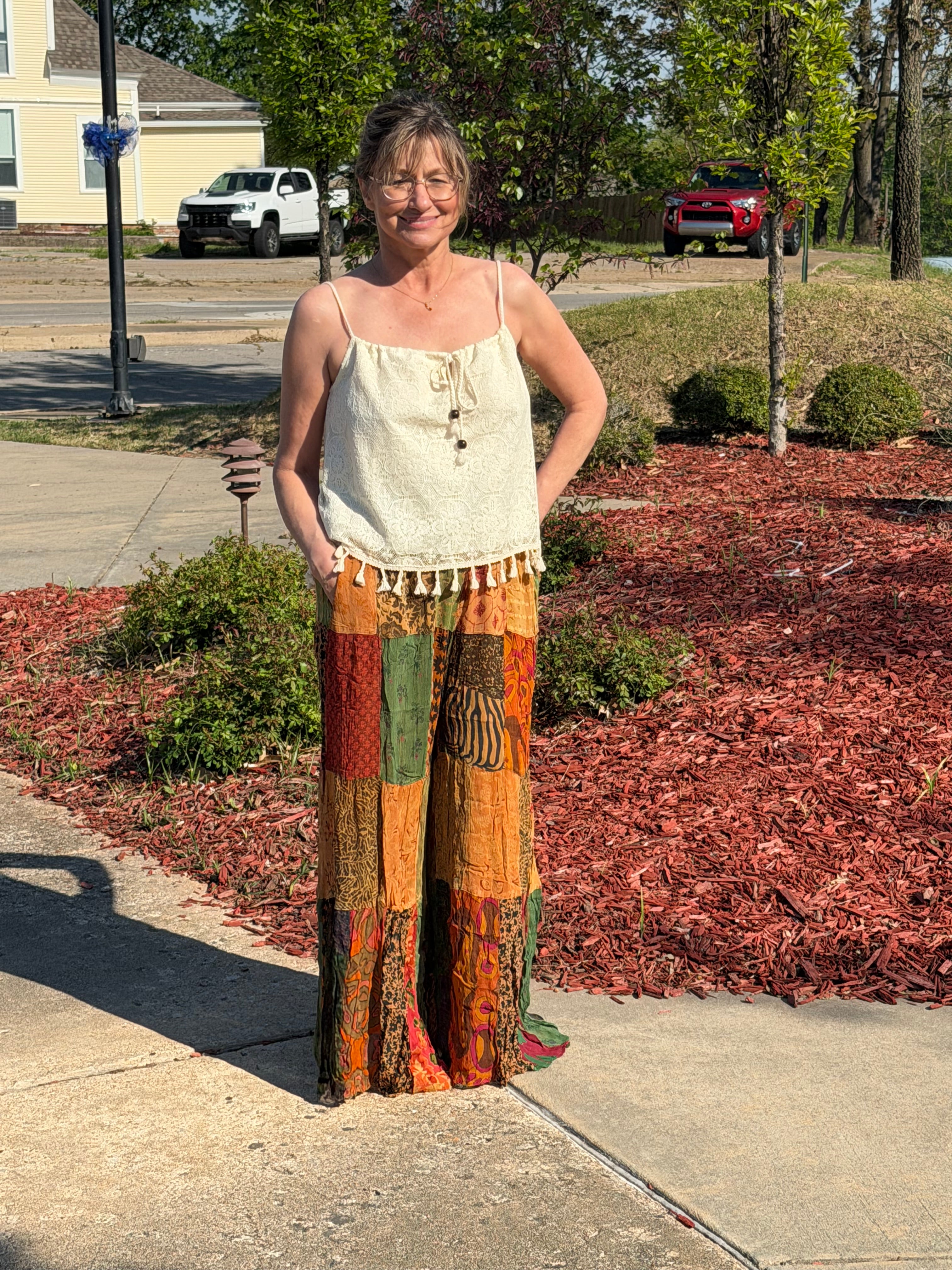 Woman wearing colorful patchwork pants and a white top in a room with decor elements.