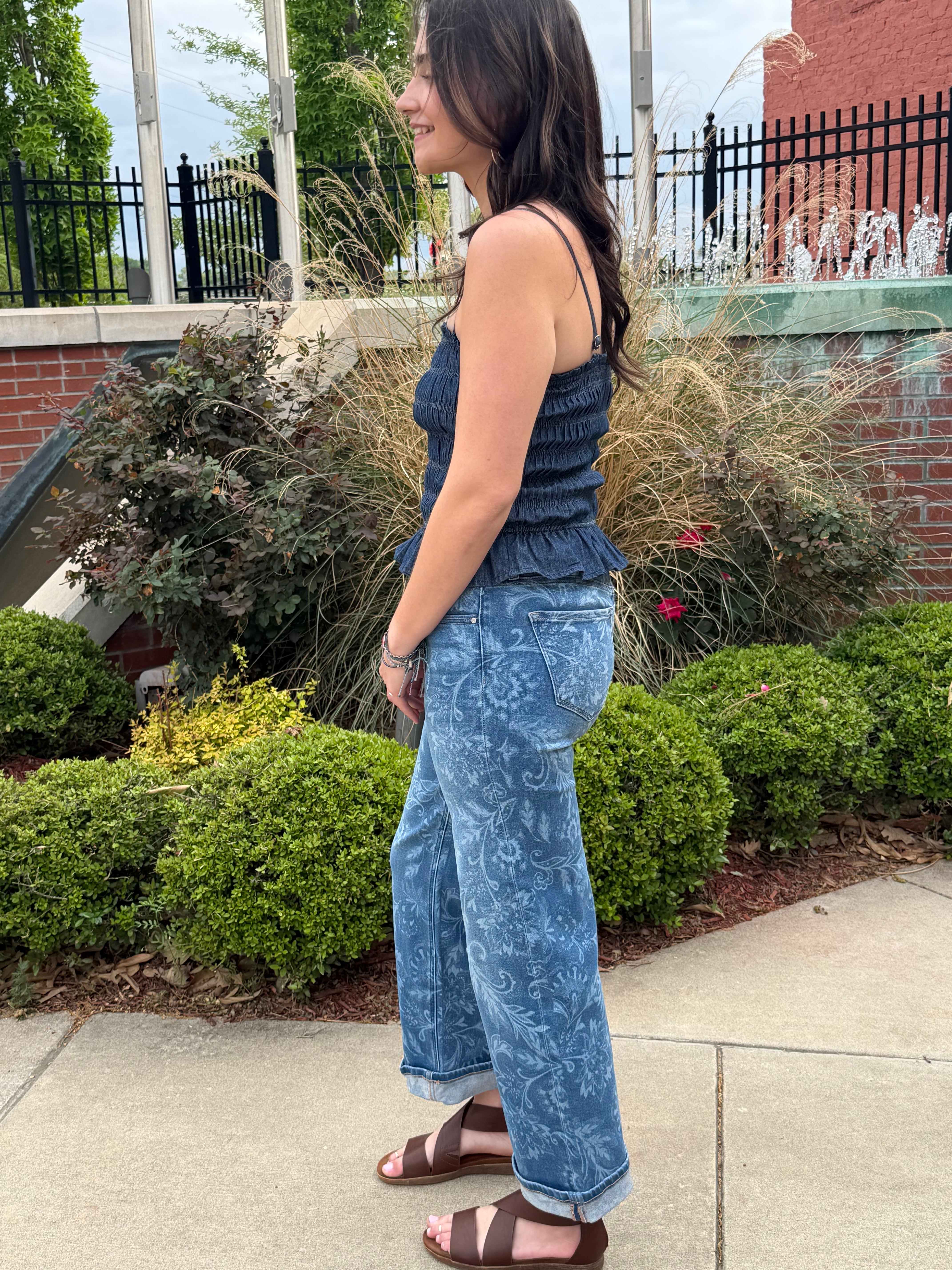 Person wearing a blue dress standing on a sidewalk with greenery in the background