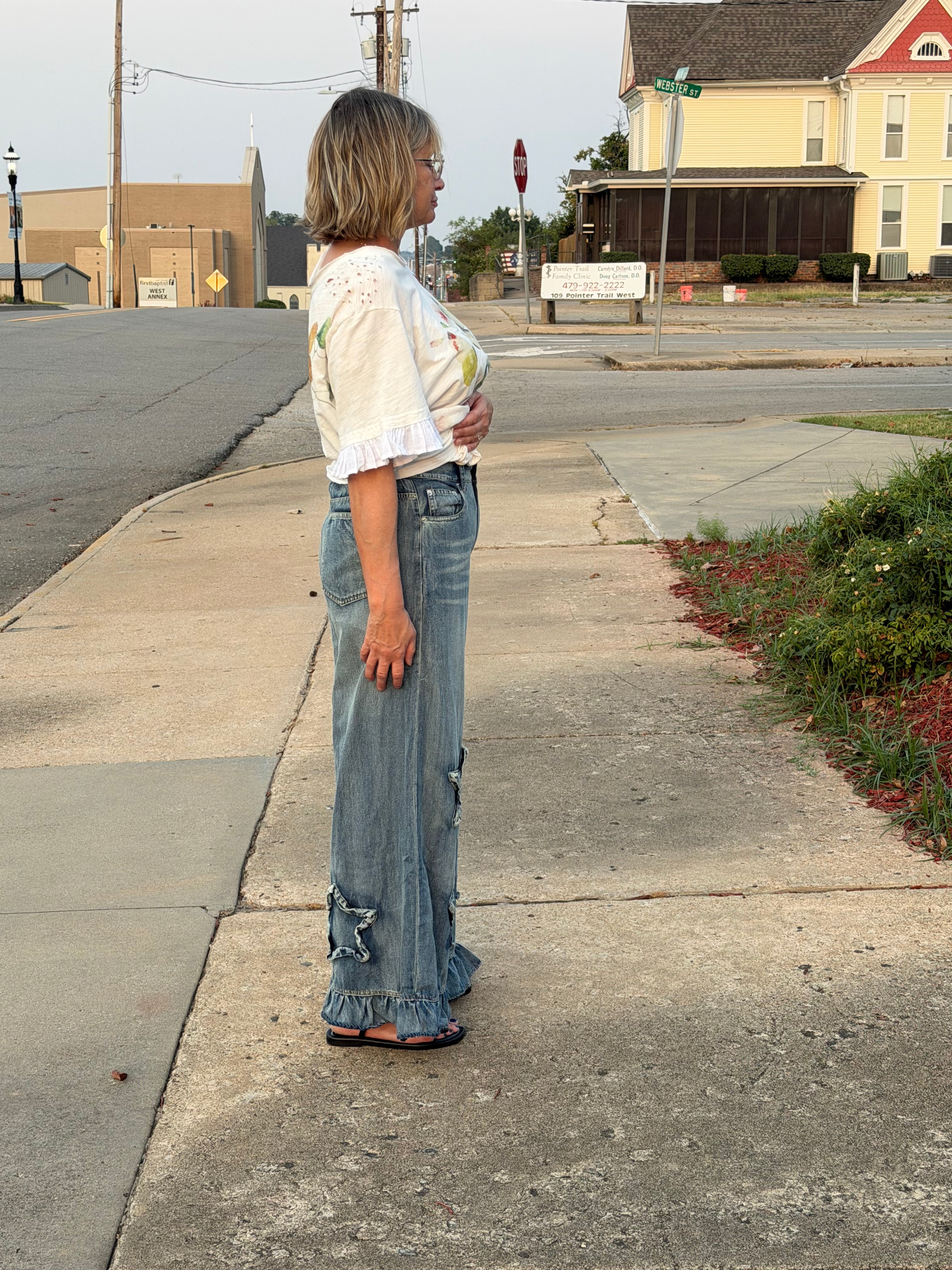 Side profile view of woman wearing Blue Velvet wide leg ruffled hem star patch denim pants showing full length silhouette
