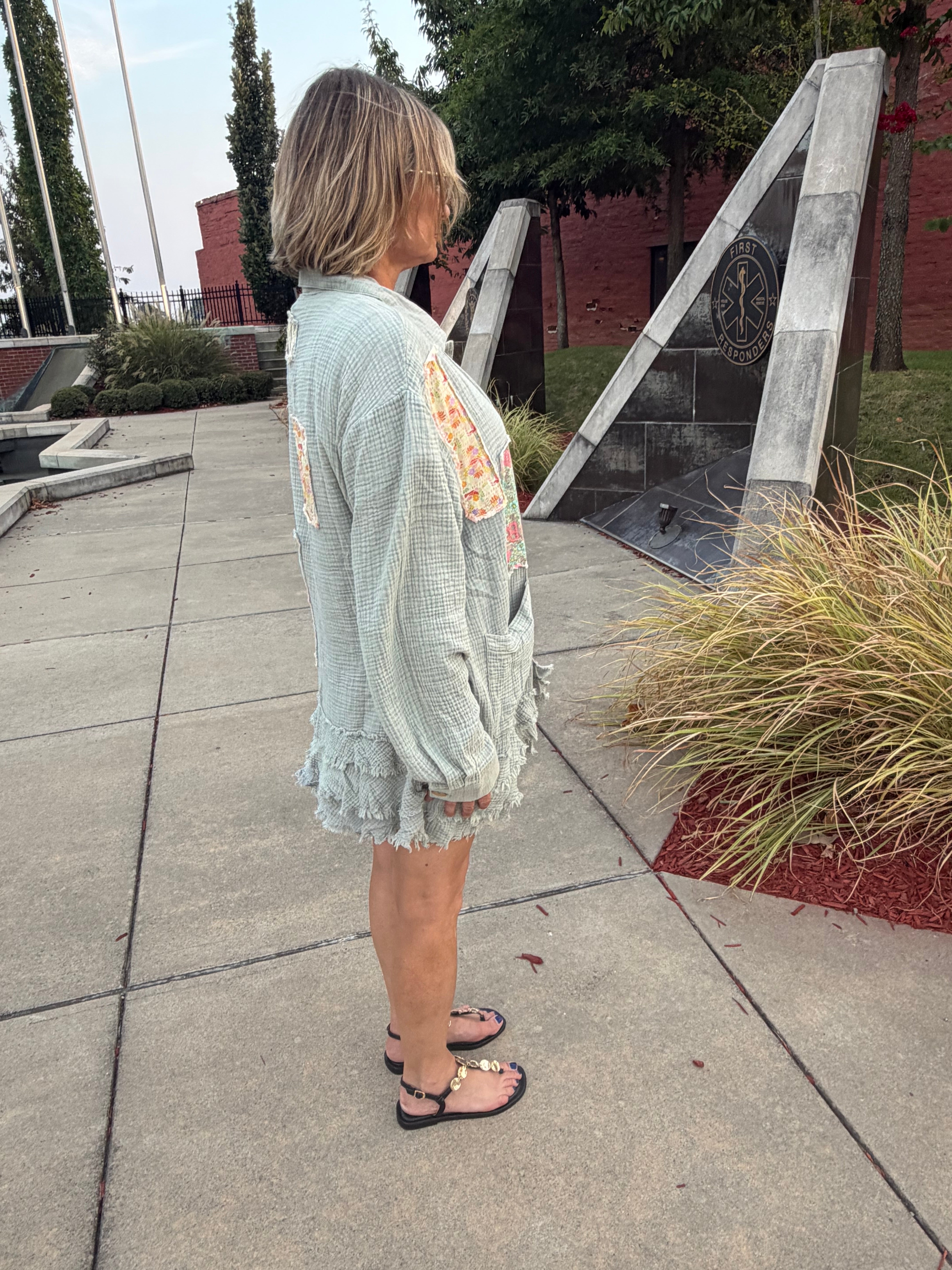 Side profile close view of Blue Velvet sage patchwork gauze shirt showing button-up sleeve cuff, patchwork panel, and layered frayed ruffle hem