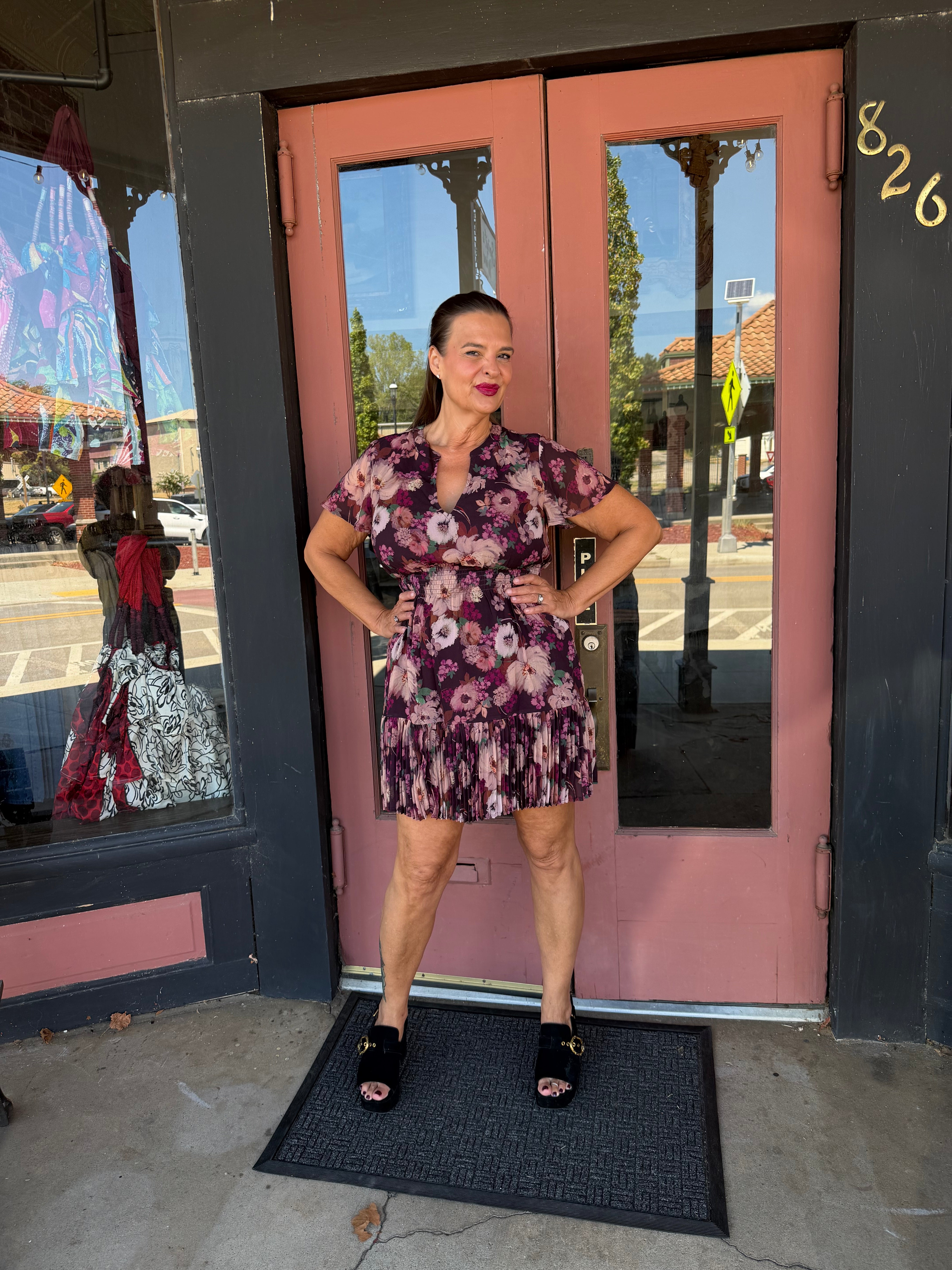 A woman wearing a short-sleeve floral mini dress with a tie waist and black platform sandals.