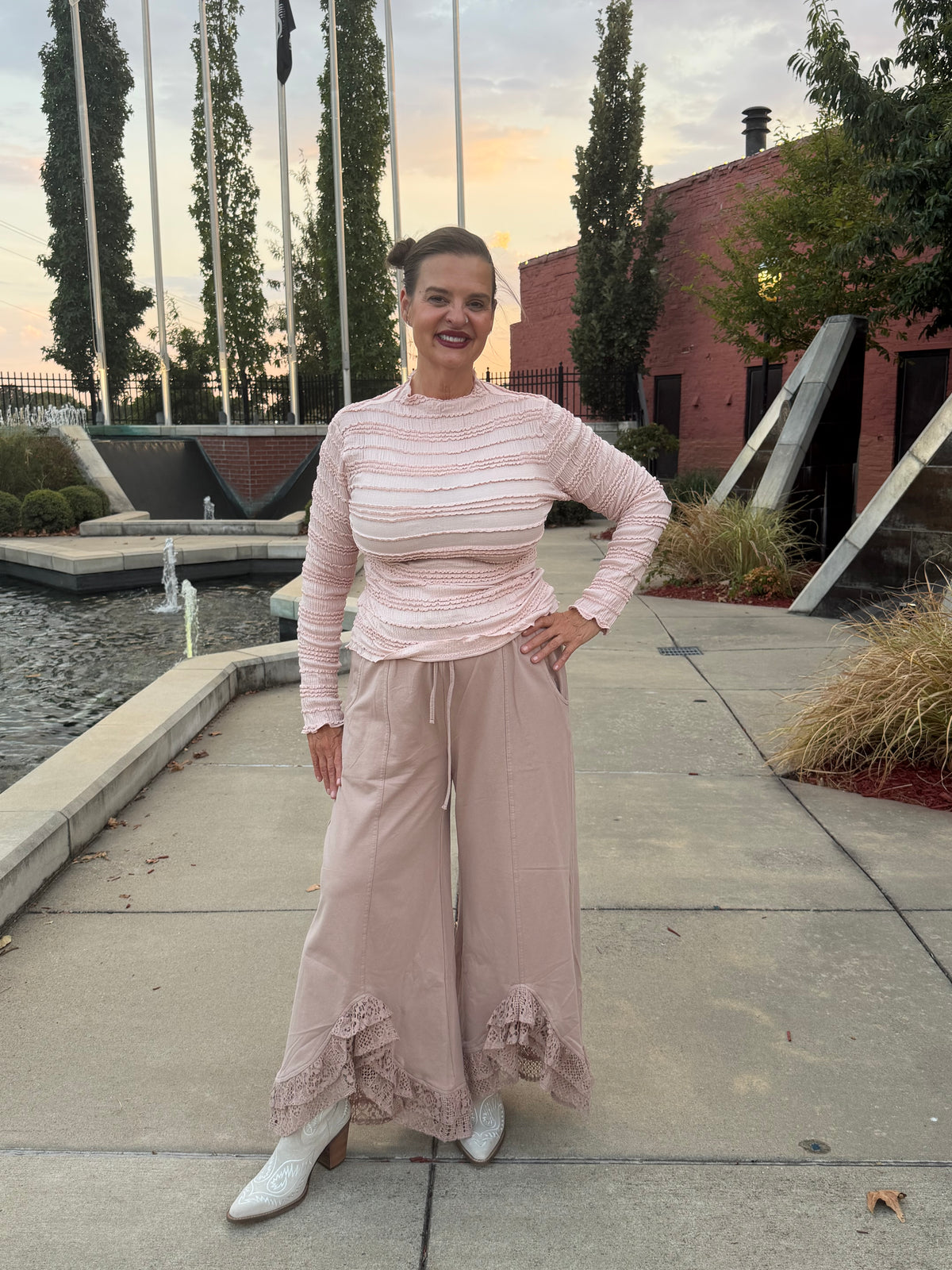 Full length fron view of Romantic Lace Mineral Wash Pants – Latte and woman in a outdoor setting wearing a soft pink ribbed knit fitted top.