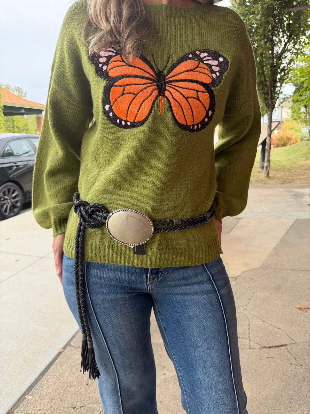 Close up view of Butterfly patchwork sweater with model wearing a leather fringe belt wrapped around with Hidden Jeans