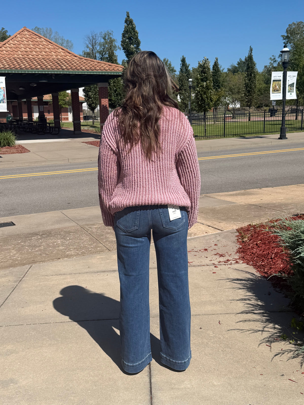 Back view of a dusty mauve ribbed sweater, showing its relaxed fit and long sleeves, styled with wide-leg jeans.