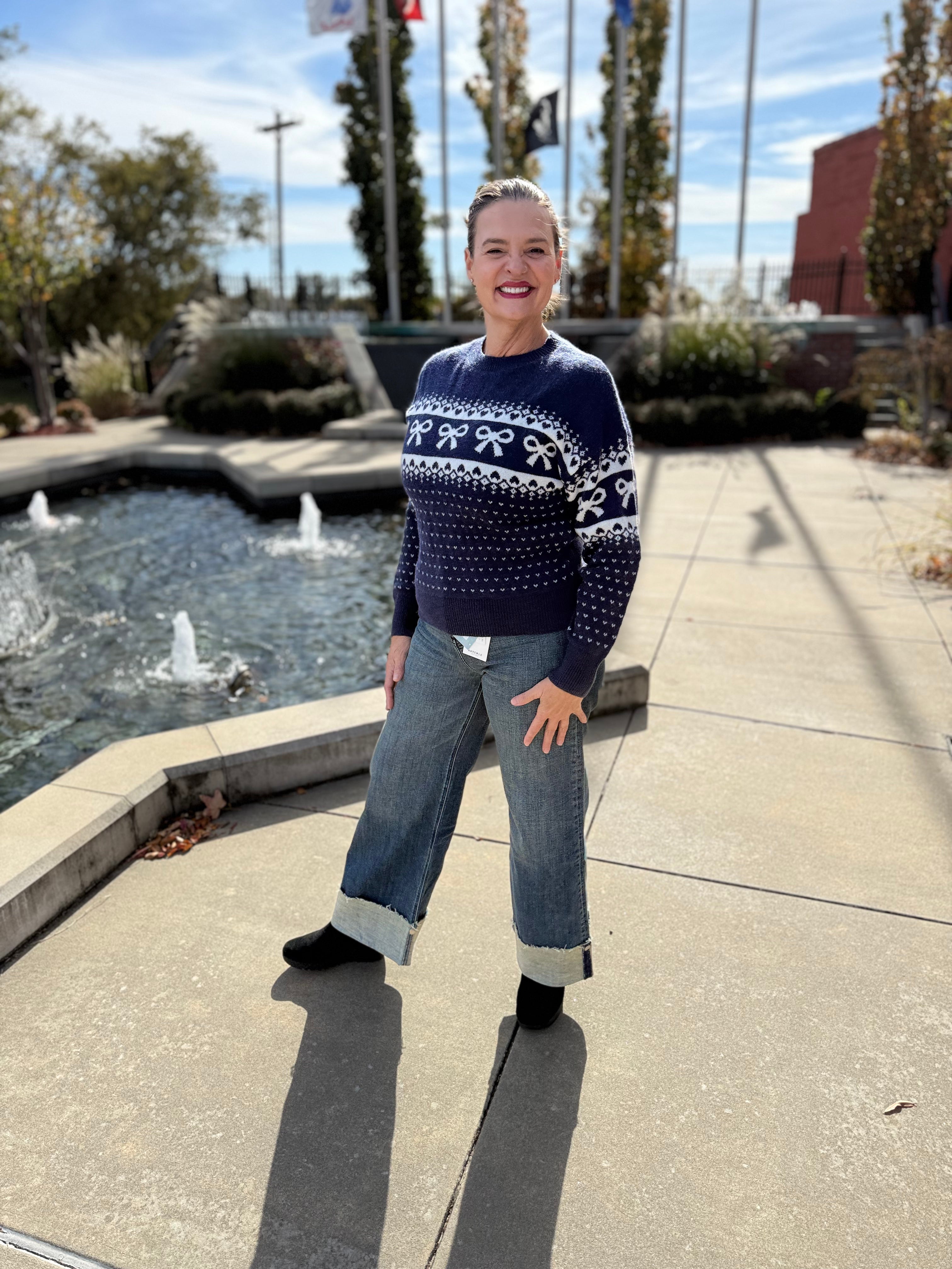 Woman wearing a patterned sweater and jeans standing by a fountain.