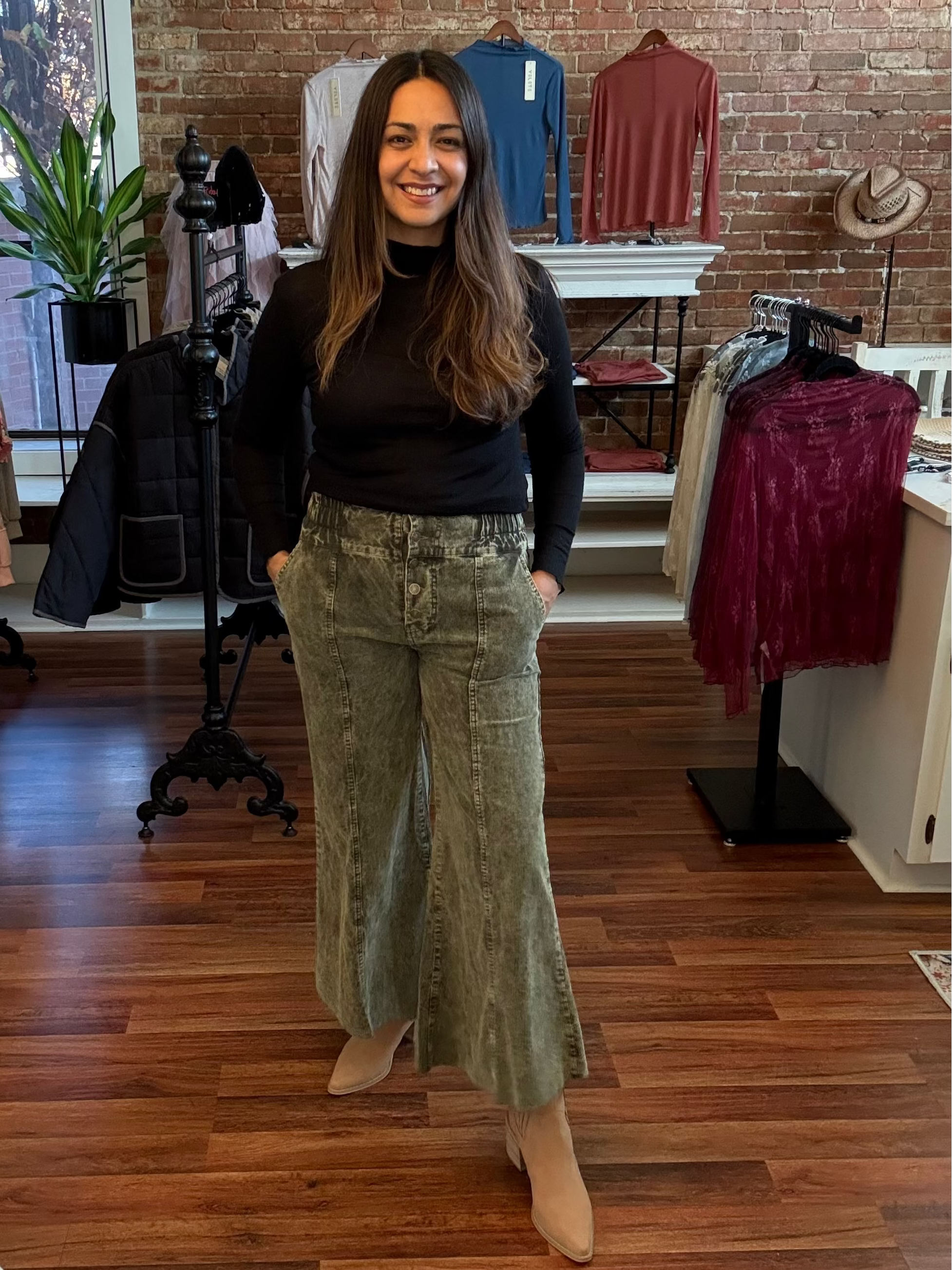 Woman standing in a clothing store wearing a black top and green corduroy pants