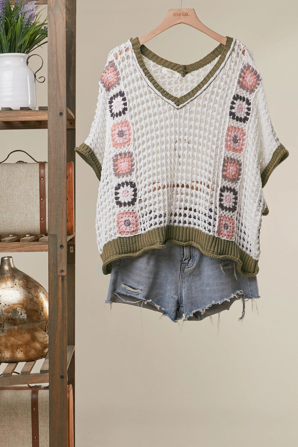 Crocheted top with geometric patterns and denim shorts on a hanger against a neutral wall.