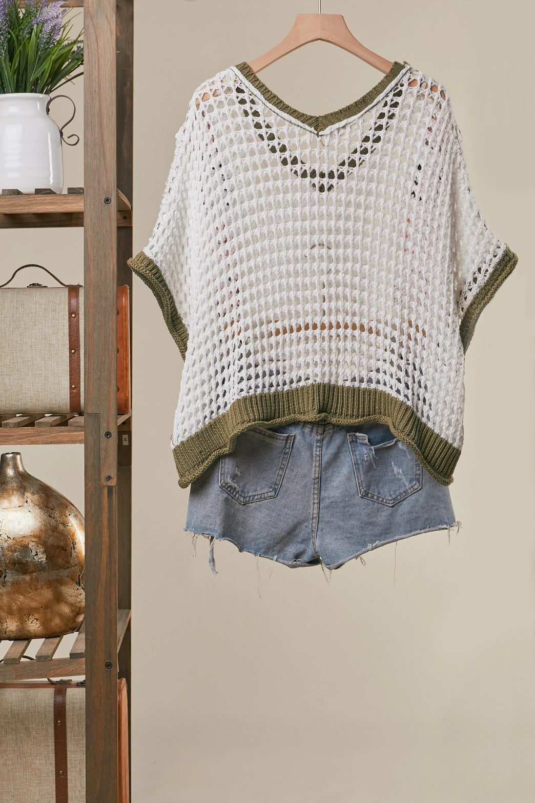 White crochet top with green trim and denim shorts on a hanger against a neutral background.