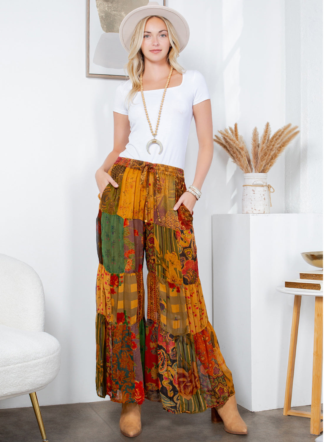 Woman wearing colorful patchwork pants and a white top in a room with decor elements.
