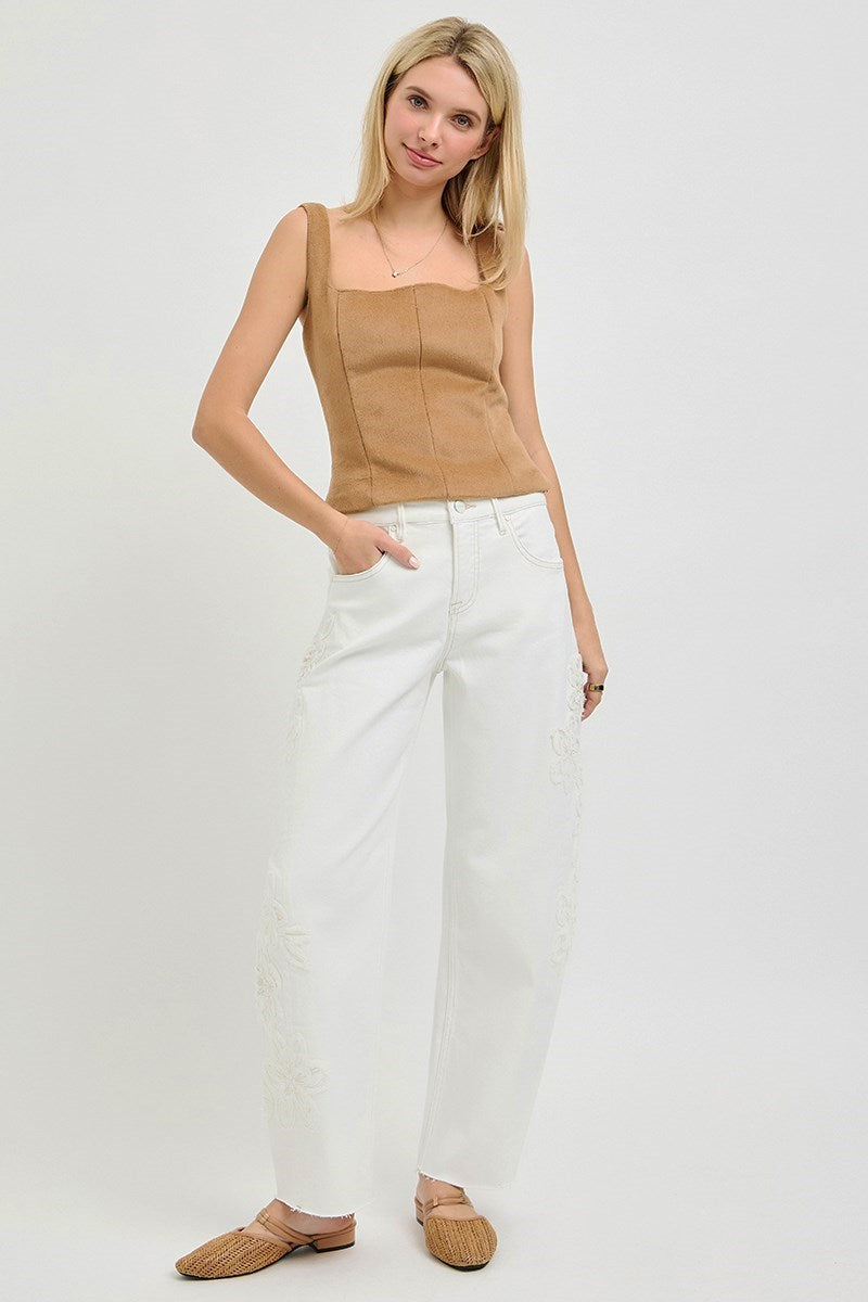 Woman wearing a beige top and white pants on a plain background