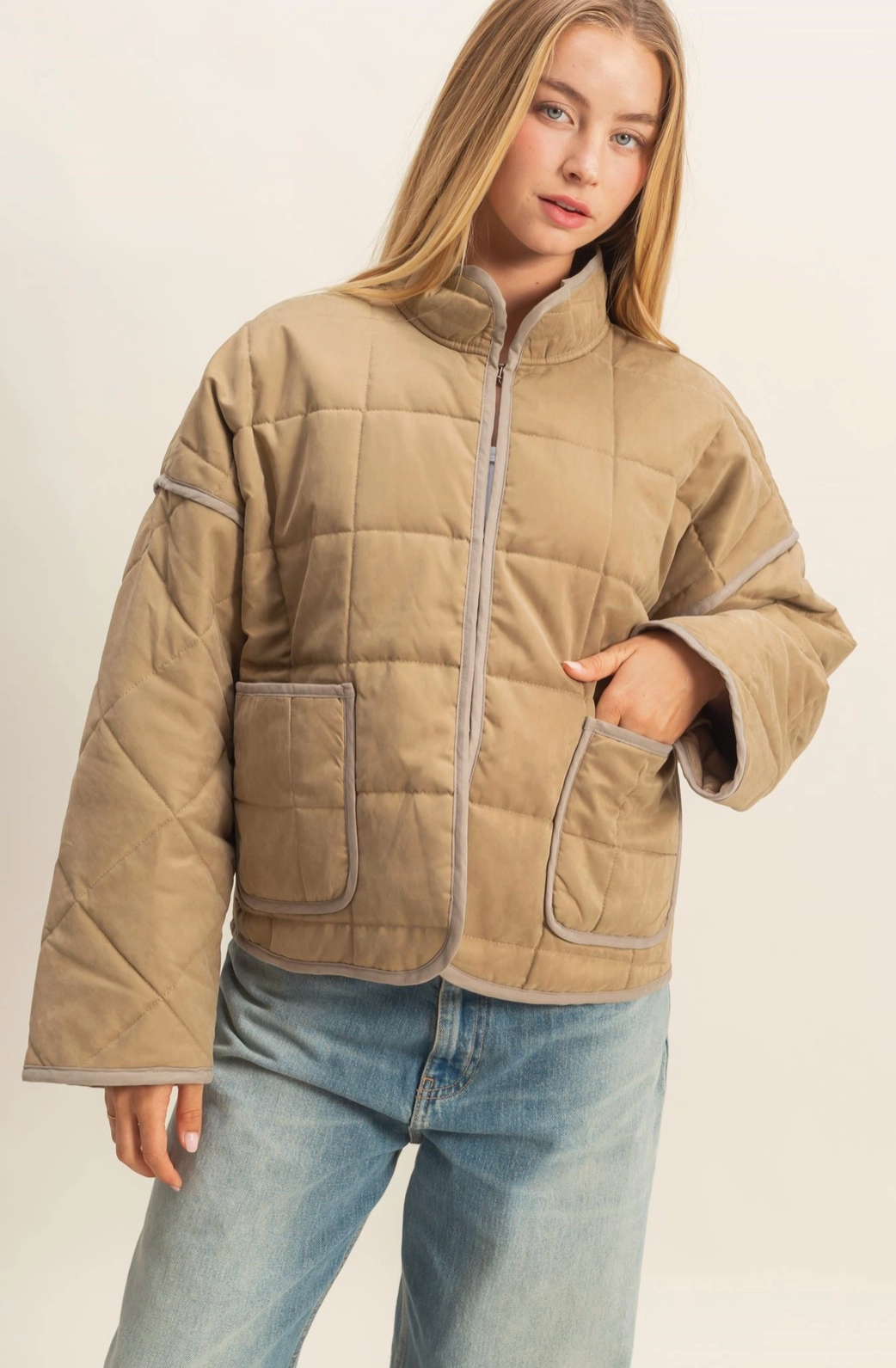 Person wearing a beige quilted jacket with a neutral background